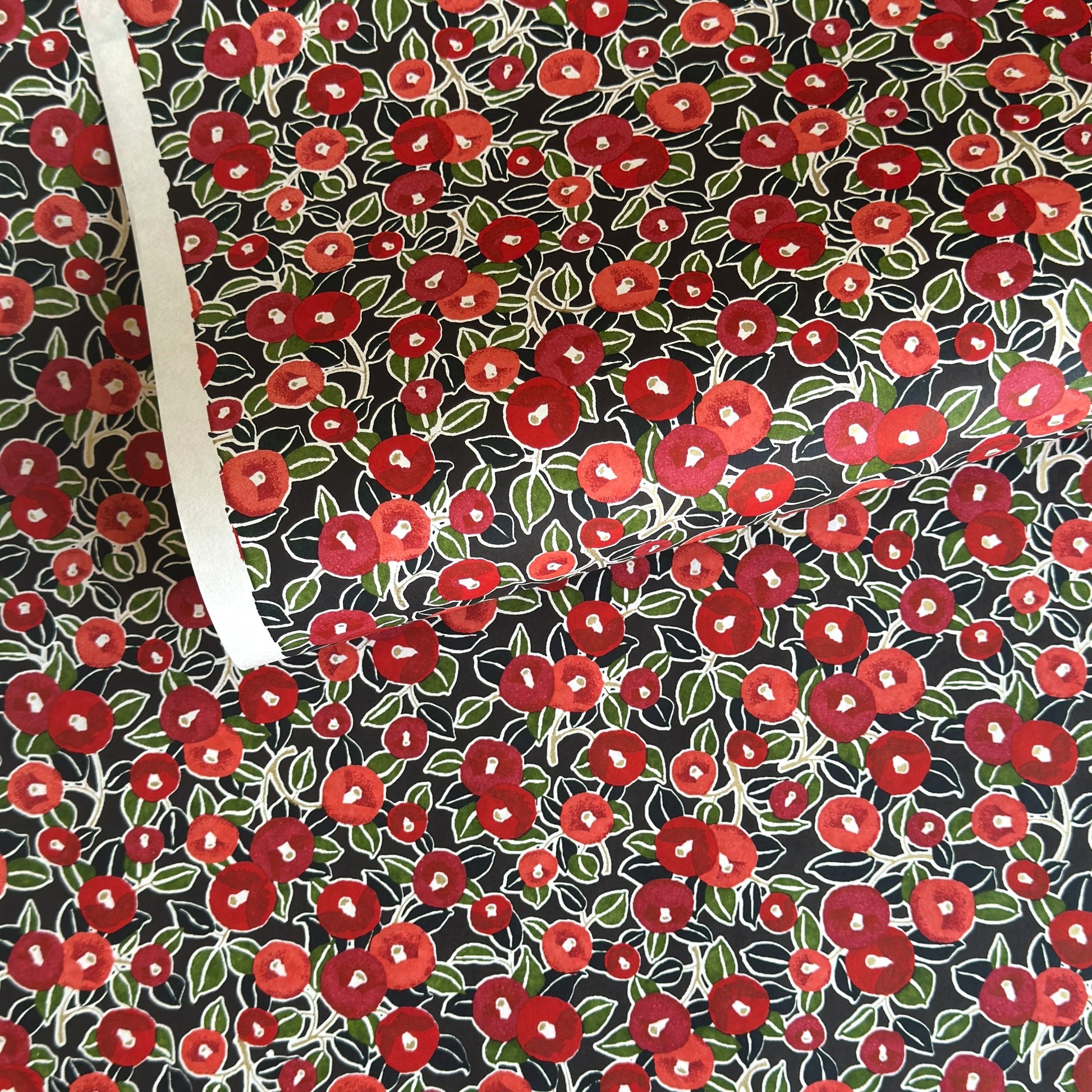 japanese silk-screen handmade paper, chiyogami, with a design showing red and pink camellia flowers and green leaves on black background