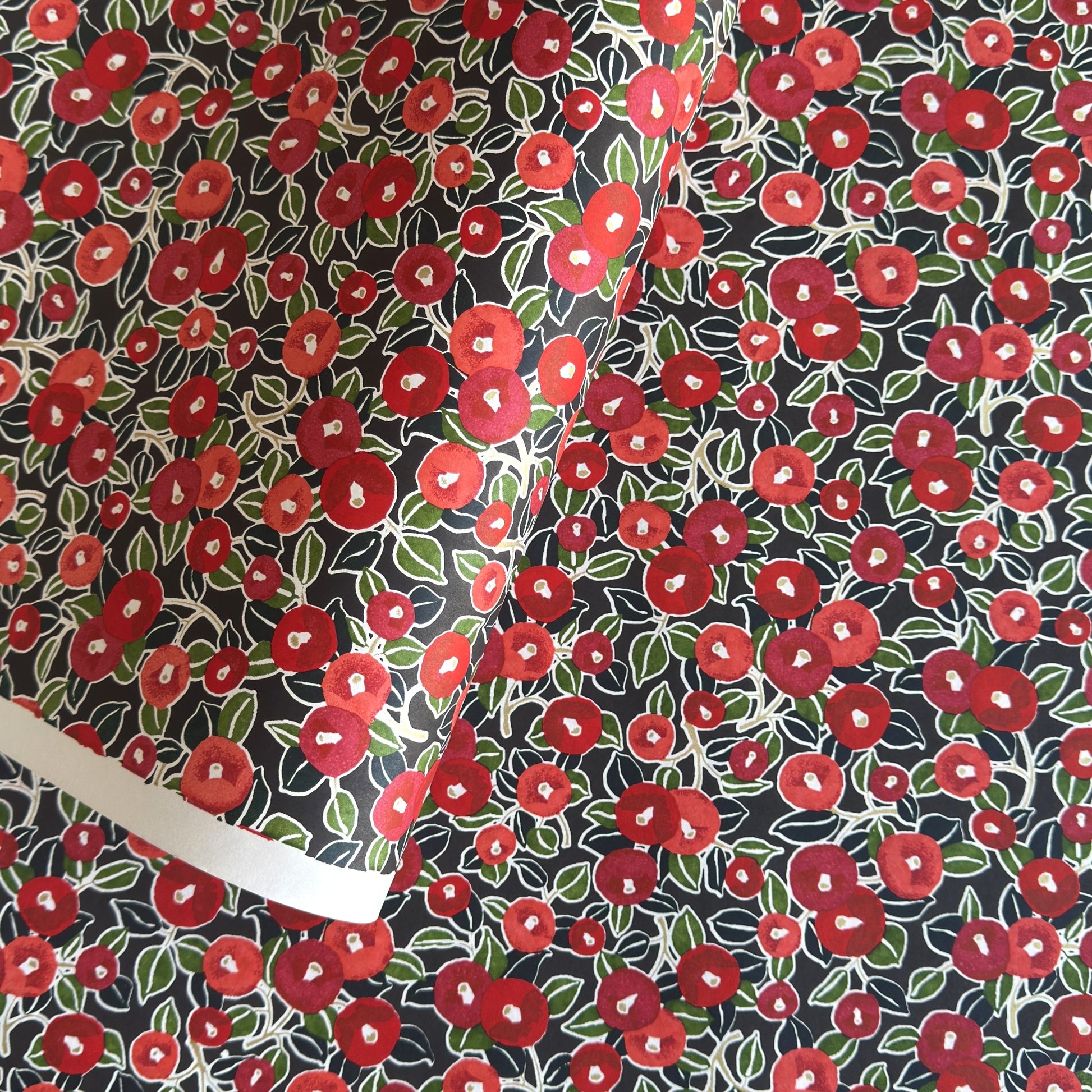 japanese silk-screen handmade paper, chiyogami, with a design showing red and pink camellia flowers and green leaves on black background