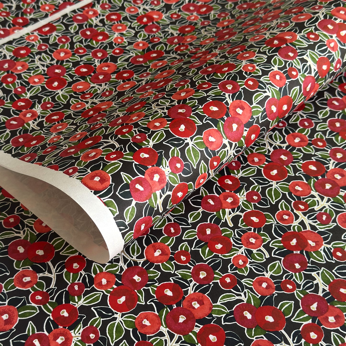 japanese silk-screen handmade paper, chiyogami, with a design showing red and pink camellia flowers and green leaves on black background