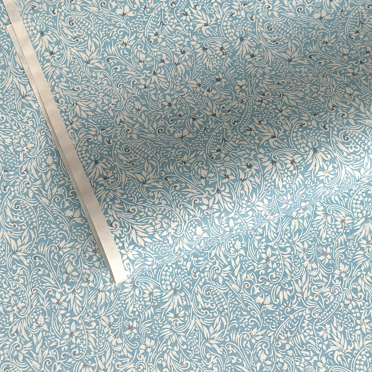 Japanese chiyogami paper - silkscreen printed - light blue backdrop with a small botanical pattern in white with silver accents.