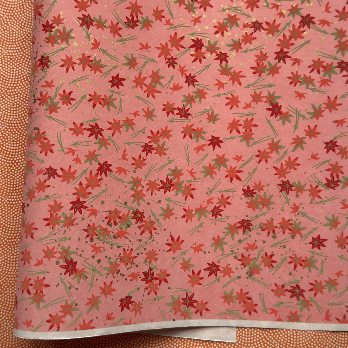 japanese silk-screen handmade paper showing pattern of red falling leaves on coral backdrop and gold highlights