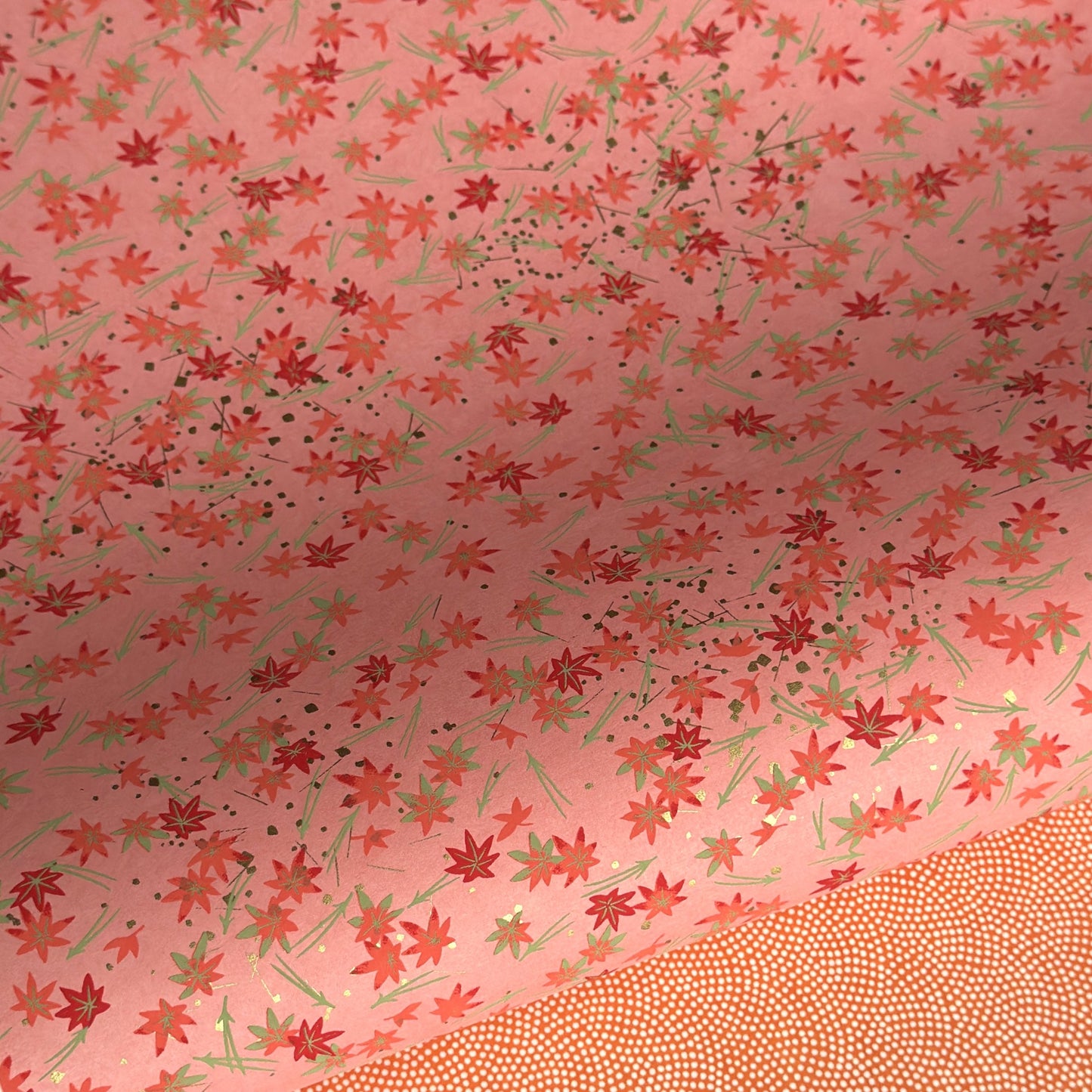 japanese silk-screen handmade paper showing pattern of red falling leaves on coral backdrop and gold highlights
