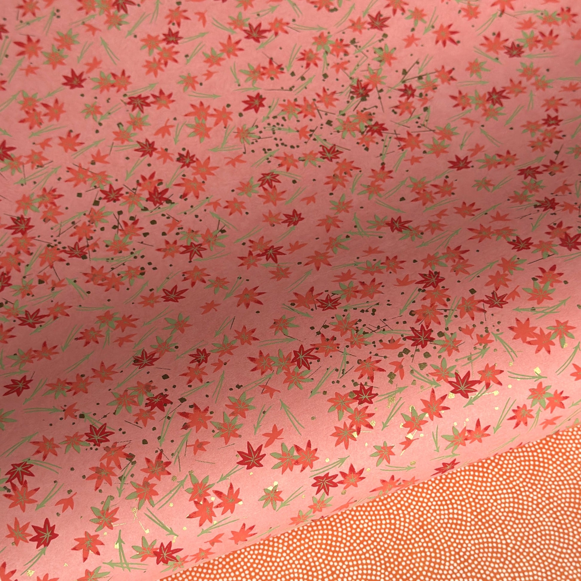 japanese silk-screen handmade paper showing pattern of red falling leaves on coral backdrop and gold highlights