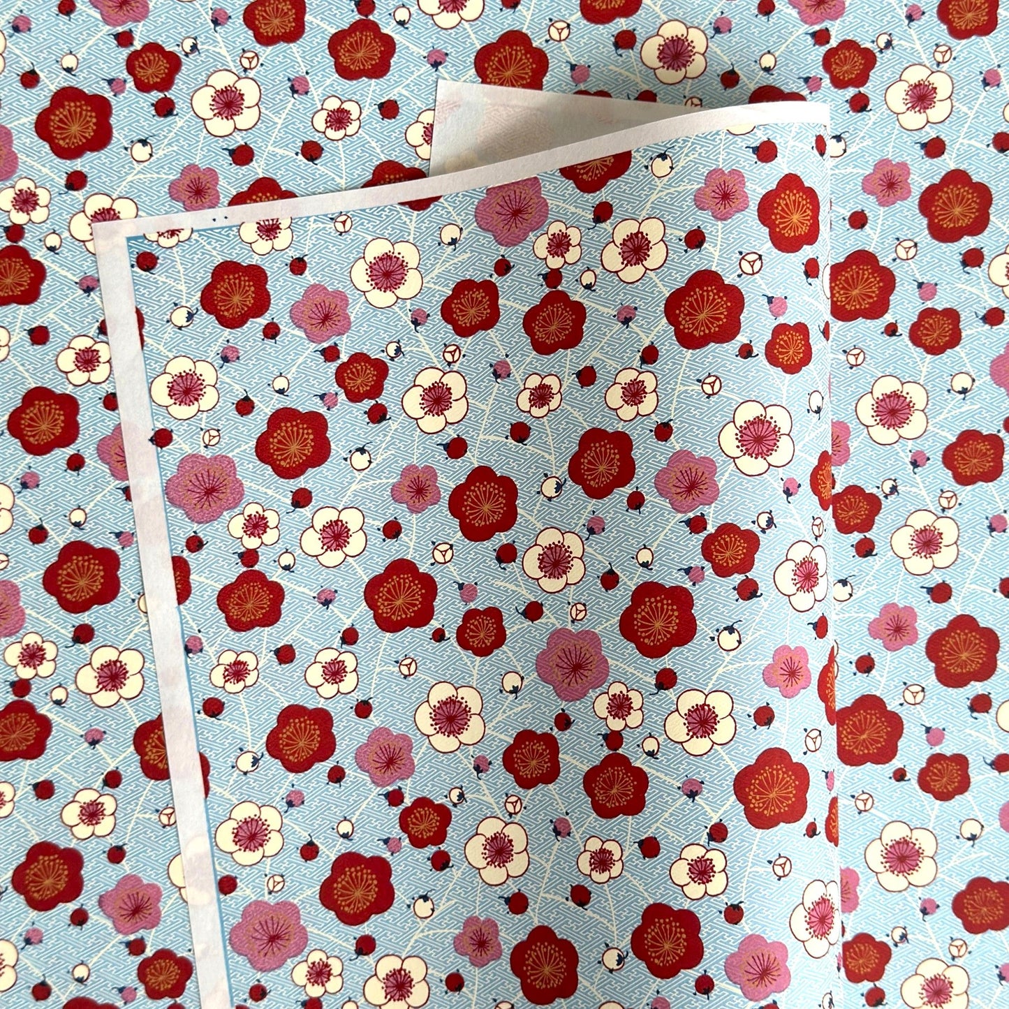 japanese silk-screen handmade paper showing red and pink plum flowers on a blue geometric backdrop