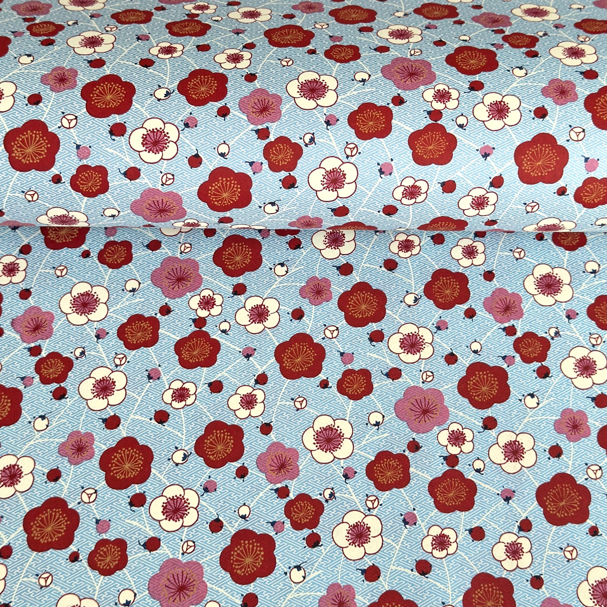 japanese silk-screen handmade paper showing red and pink plum flowers on a blue geometric backdrop