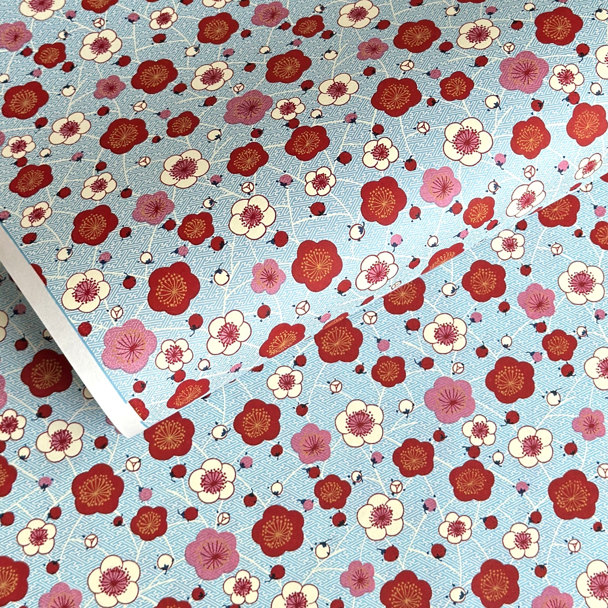japanese silk-screen handmade paper showing red and pink plum flowers on a blue geometric backdrop