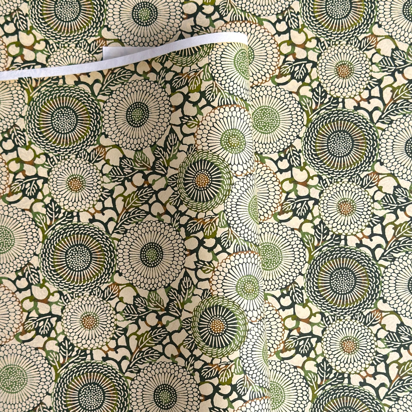 Japanese silkscreen chiyogami paper with a repeat pattern of stylised chrysanthemum flowers in tones of deep green on a buttermilk cream backdrop.