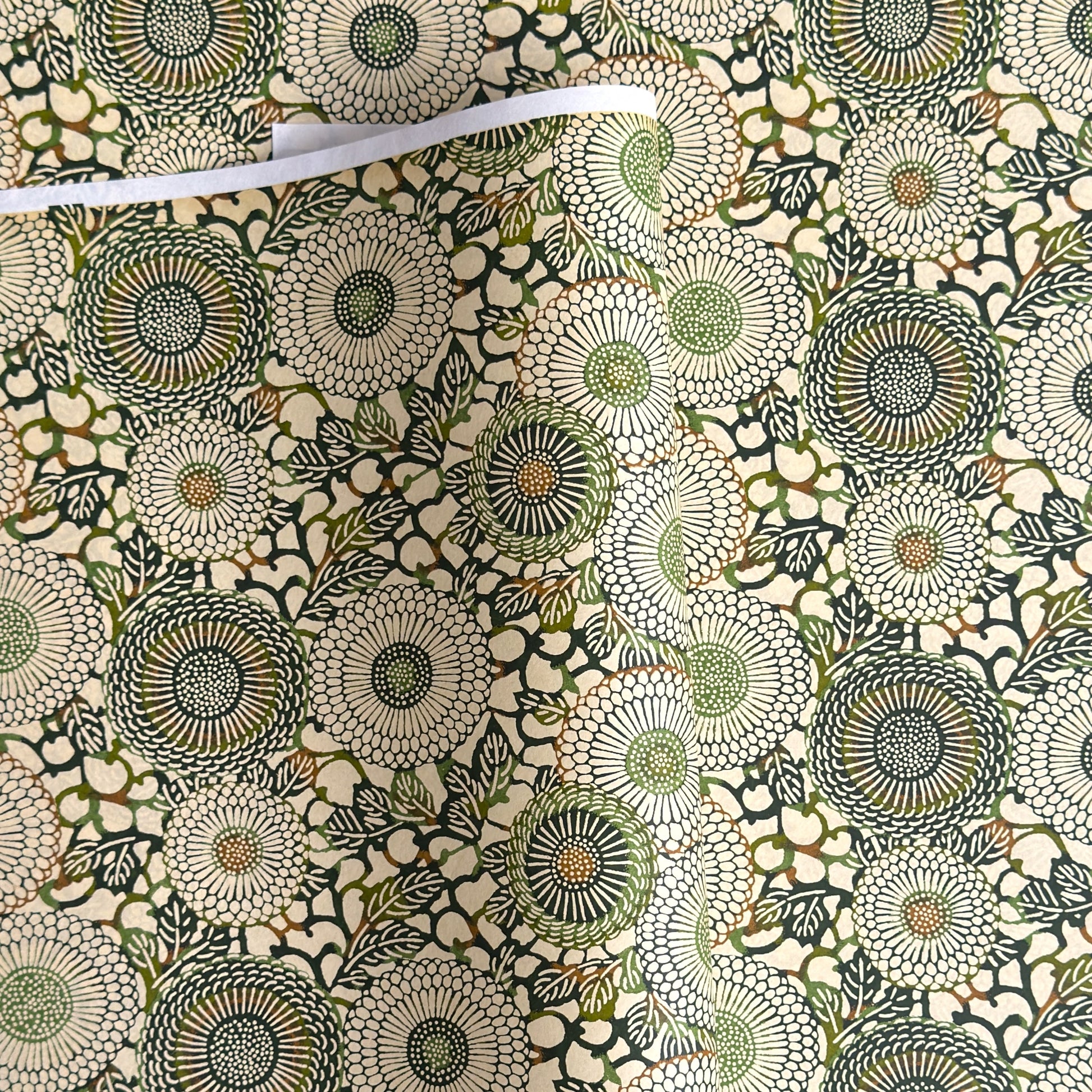 Japanese silkscreen chiyogami paper with a repeat pattern of stylised chrysanthemum flowers in tones of deep green on a buttermilk cream backdrop.