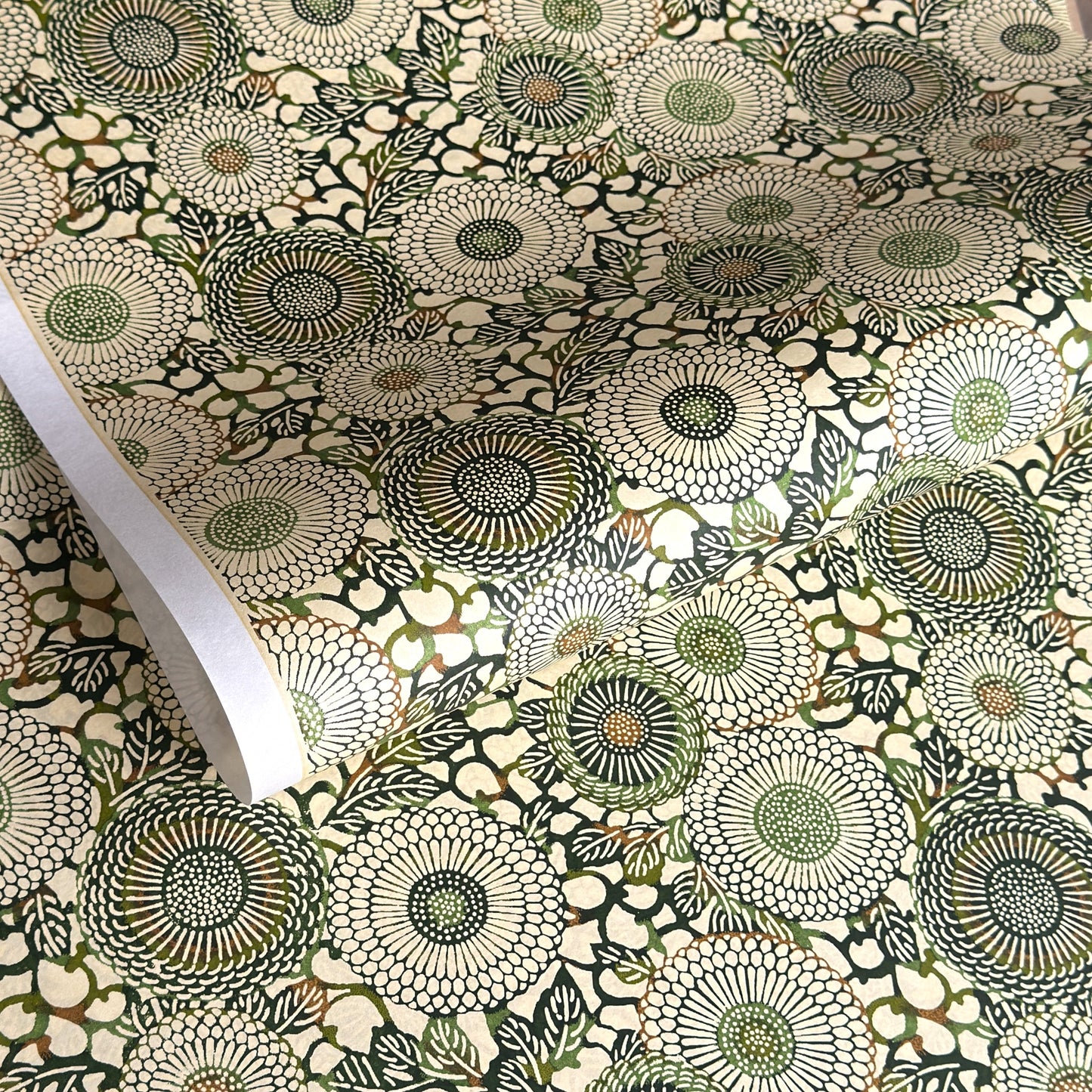 Japanese silkscreen chiyogami paper with a repeat pattern of stylised chrysanthemum flowers in tones of deep green on a buttermilk cream backdrop.