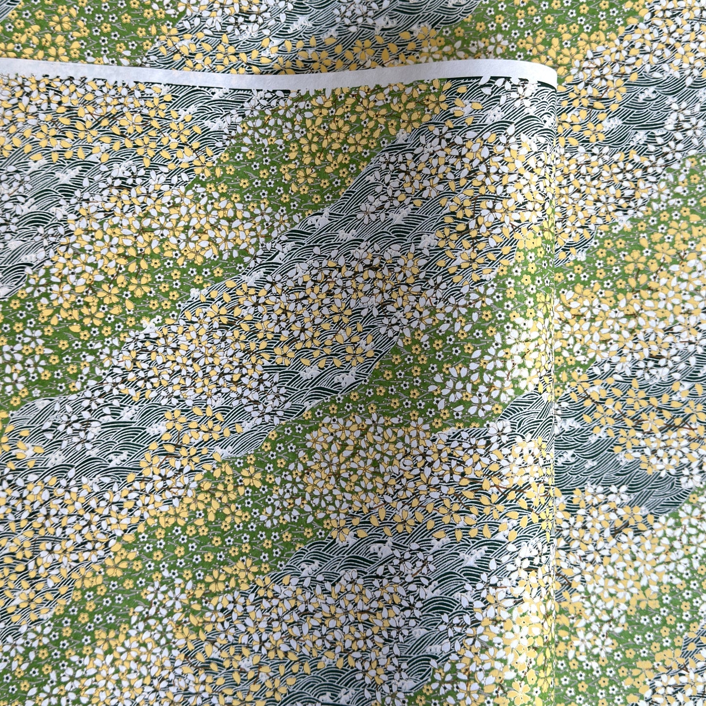 Japanese silkscreen chiyogami paper with a pattern of dark green rivers and grass green banks with an abundance of little flowers in white and yellow