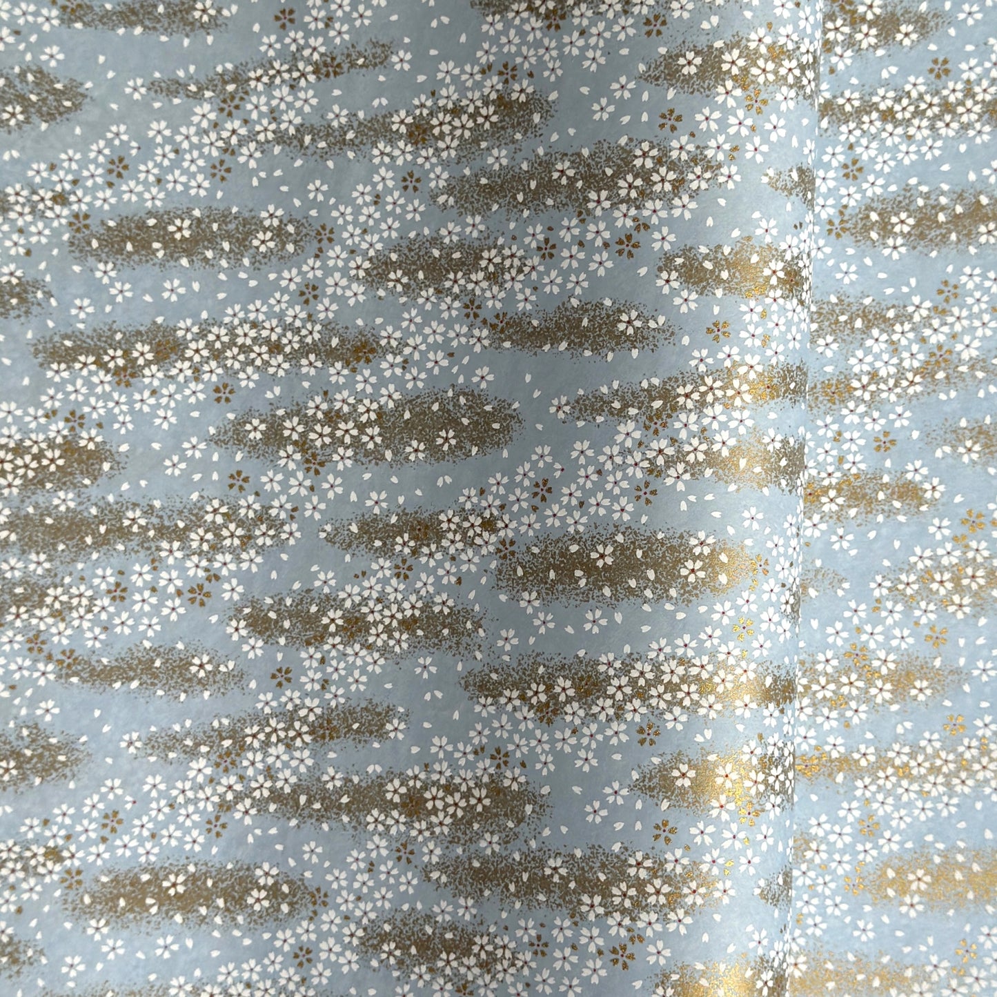 a sheet of Japanese silkscreen printed chiyogami paper with waves of tiny white and gold flowers on a soft aqua background with a dusting of gold.