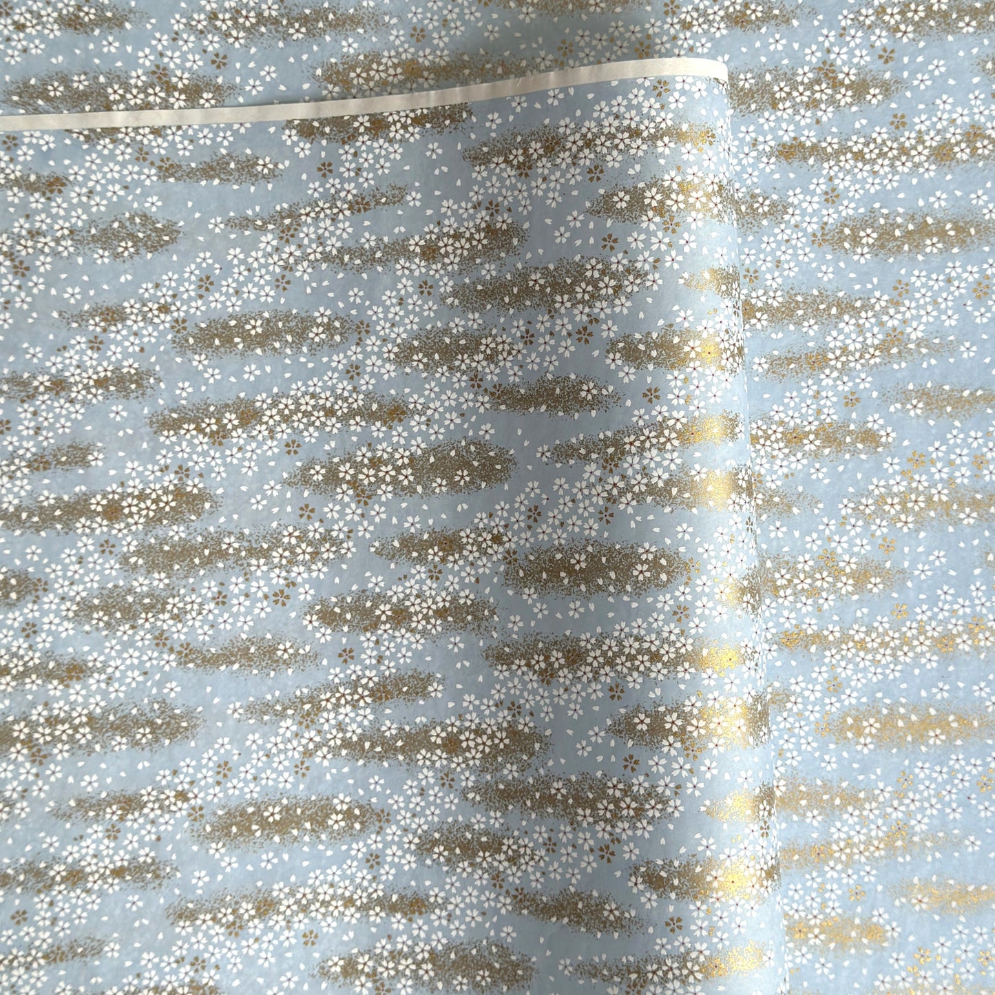 a sheet of Japanese silkscreen printed chiyogami paper with waves of tiny white and gold flowers on a soft aqua background with a dusting of gold.