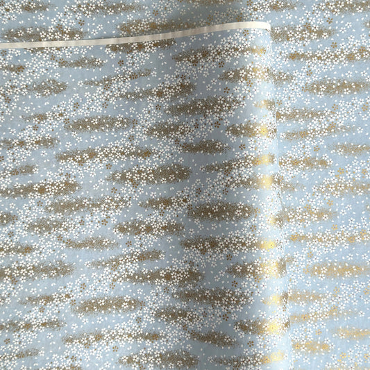 a sheet of Japanese silkscreen printed chiyogami paper with waves of tiny white and gold flowers on a soft aqua background with a dusting of gold.
