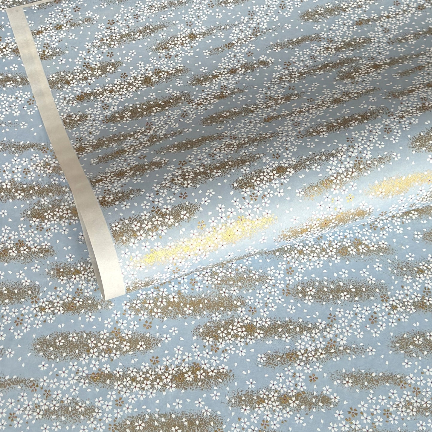 a sheet of Japanese silkscreen printed chiyogami paper with waves of tiny white and gold flowers on a soft aqua background with a dusting of gold.