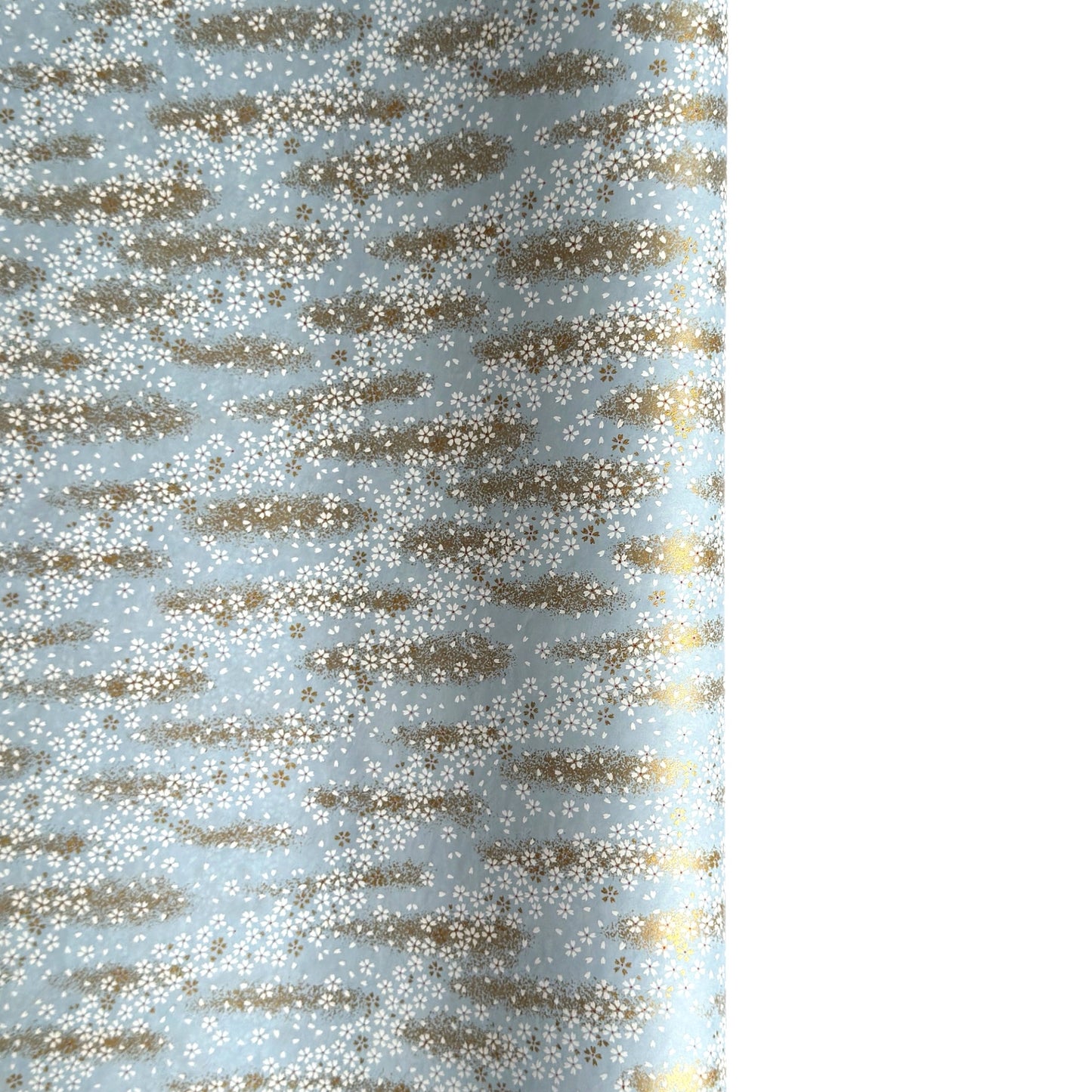 a sheet of Japanese silkscreen printed chiyogami paper with waves of tiny white and gold flowers on a soft aqua background with a dusting of gold.