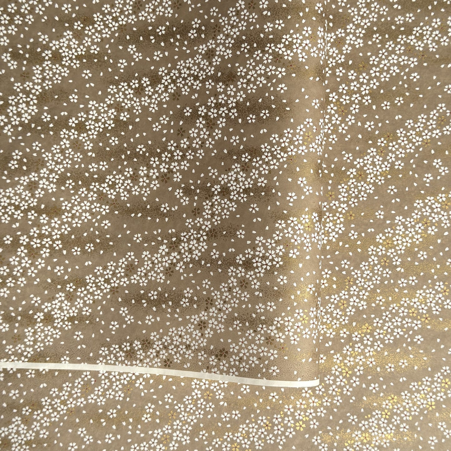 a sheet of Japanese silkscreen printed chiyogami paper with waves of tiny white and gold flowers on a soft taupe background with a dusting of gold.