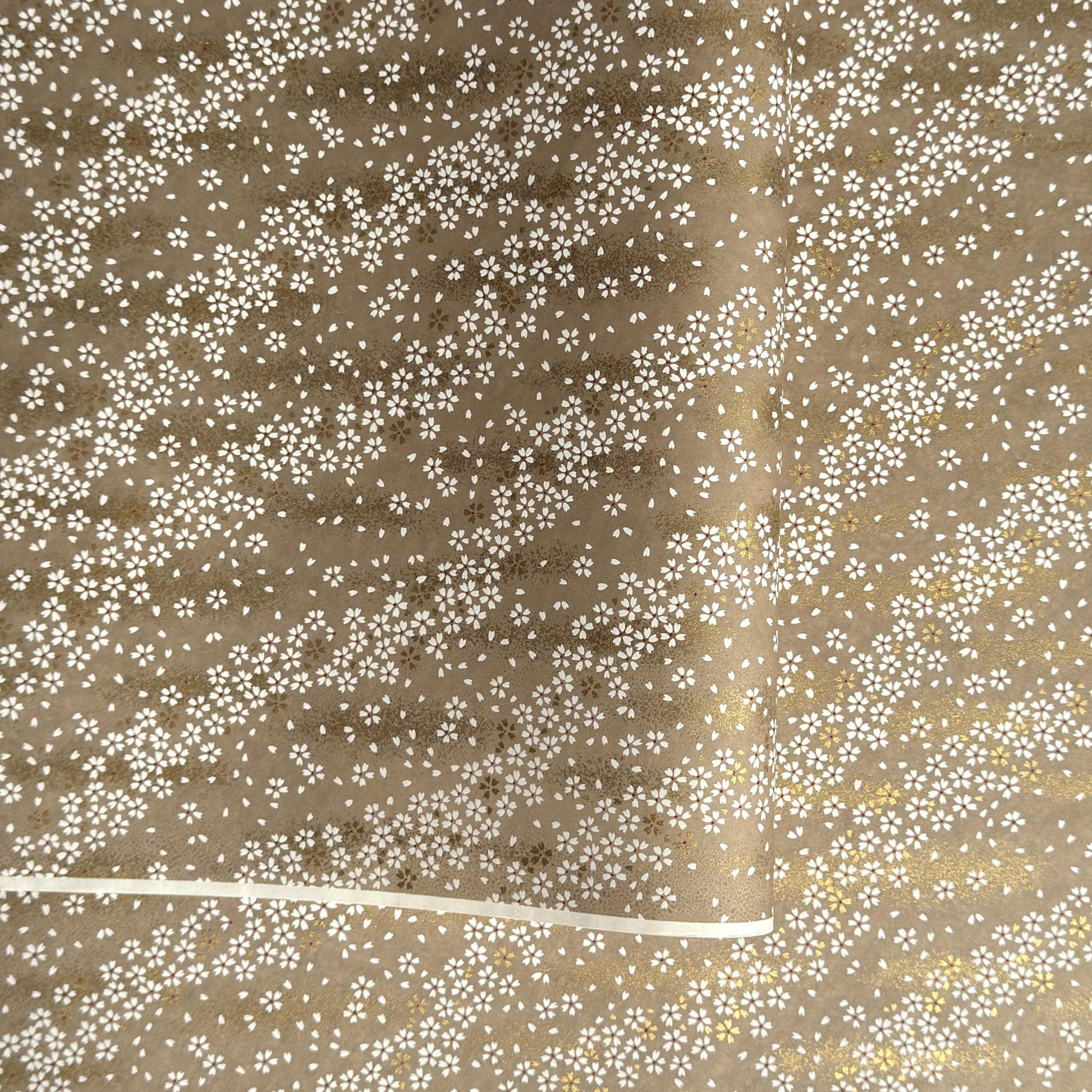 a sheet of Japanese silkscreen printed chiyogami paper with waves of tiny white and gold flowers on a soft taupe background with a dusting of gold.