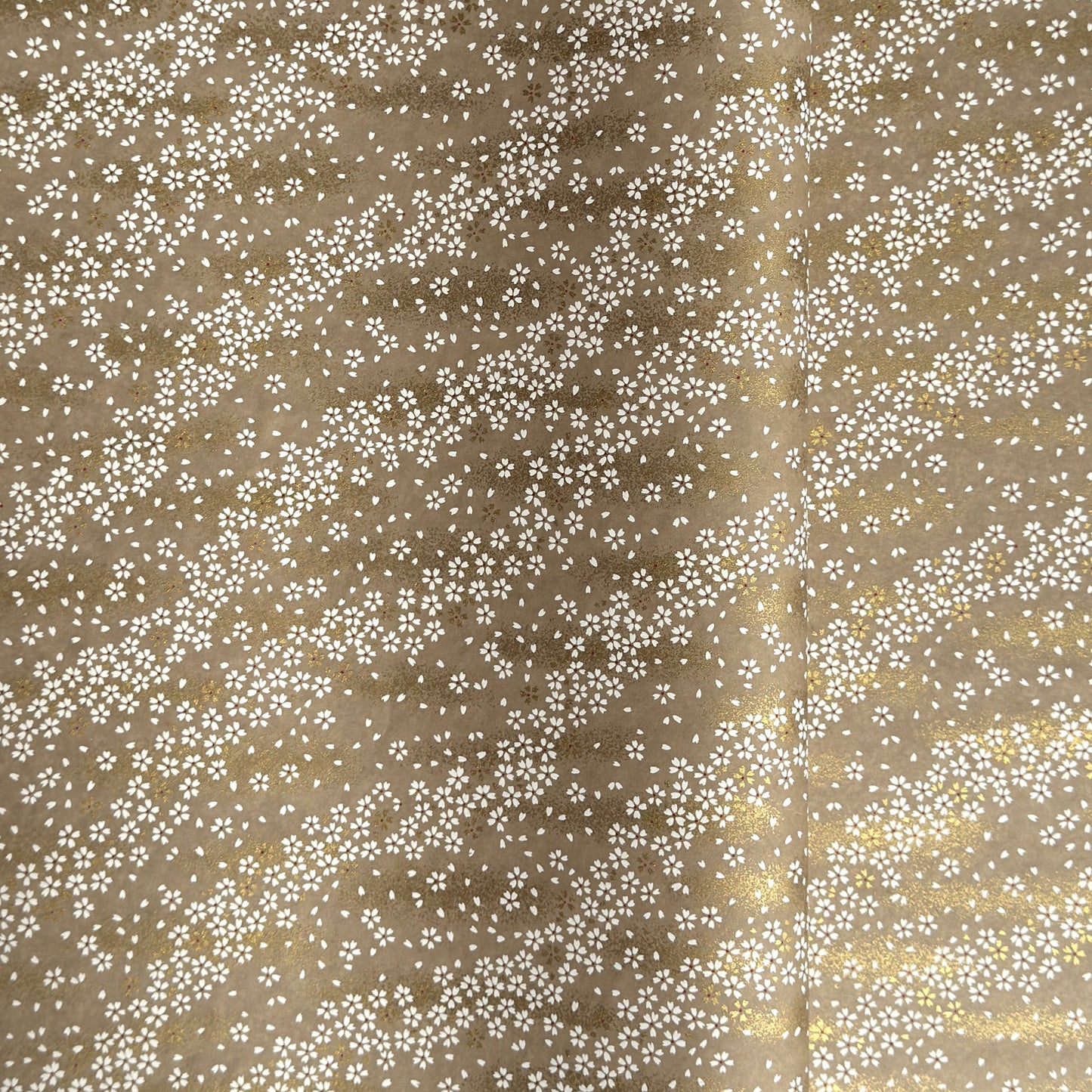 a sheet of Japanese silkscreen printed chiyogami paper with waves of tiny white and gold flowers on a soft taupe background with a dusting of gold.