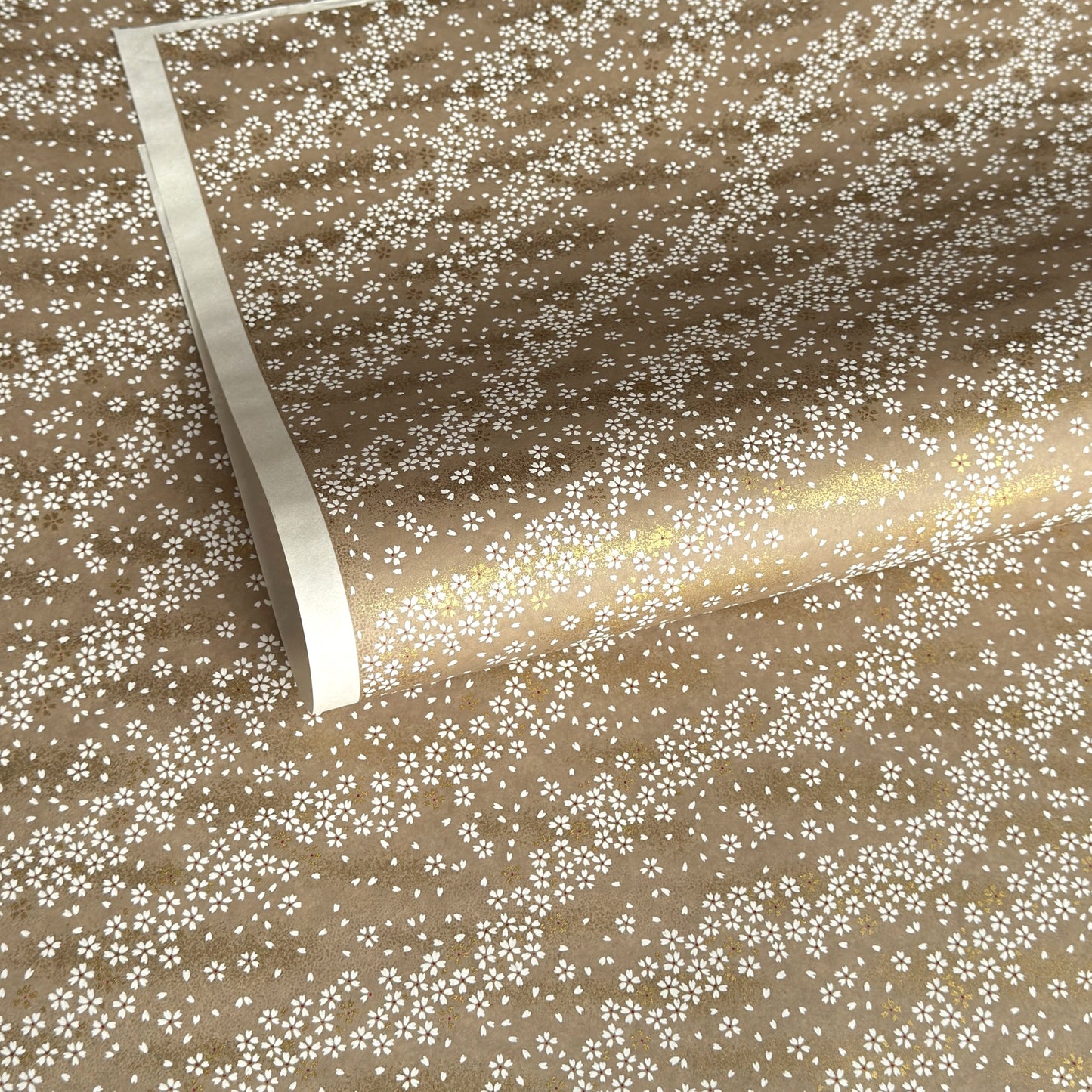 a sheet of Japanese silkscreen printed chiyogami paper with waves of tiny white and gold flowers on a soft taupe background with a dusting of gold.