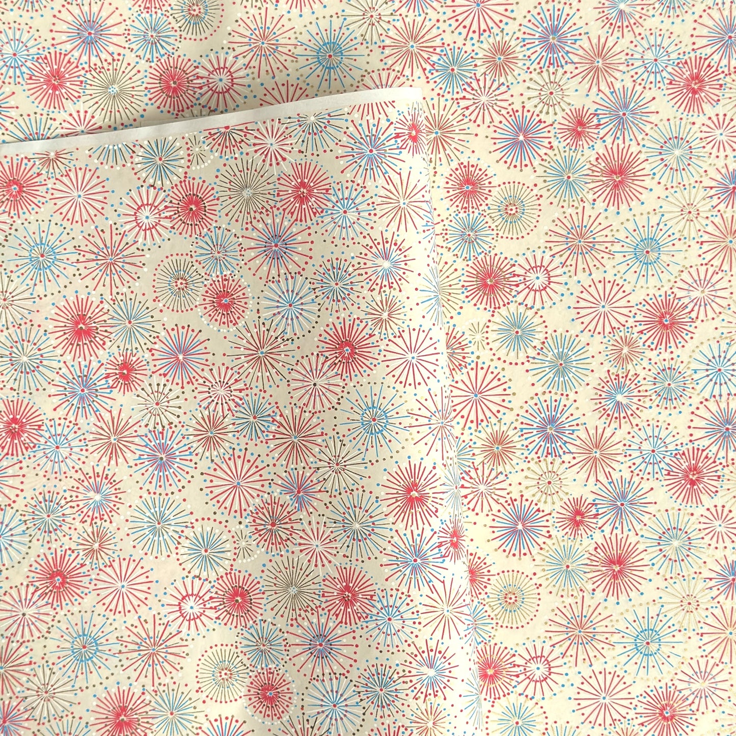japanese chiyogami silkscreen printed paper with a pattern of fireworks in reds, pinks and lilacs on an ivory background.