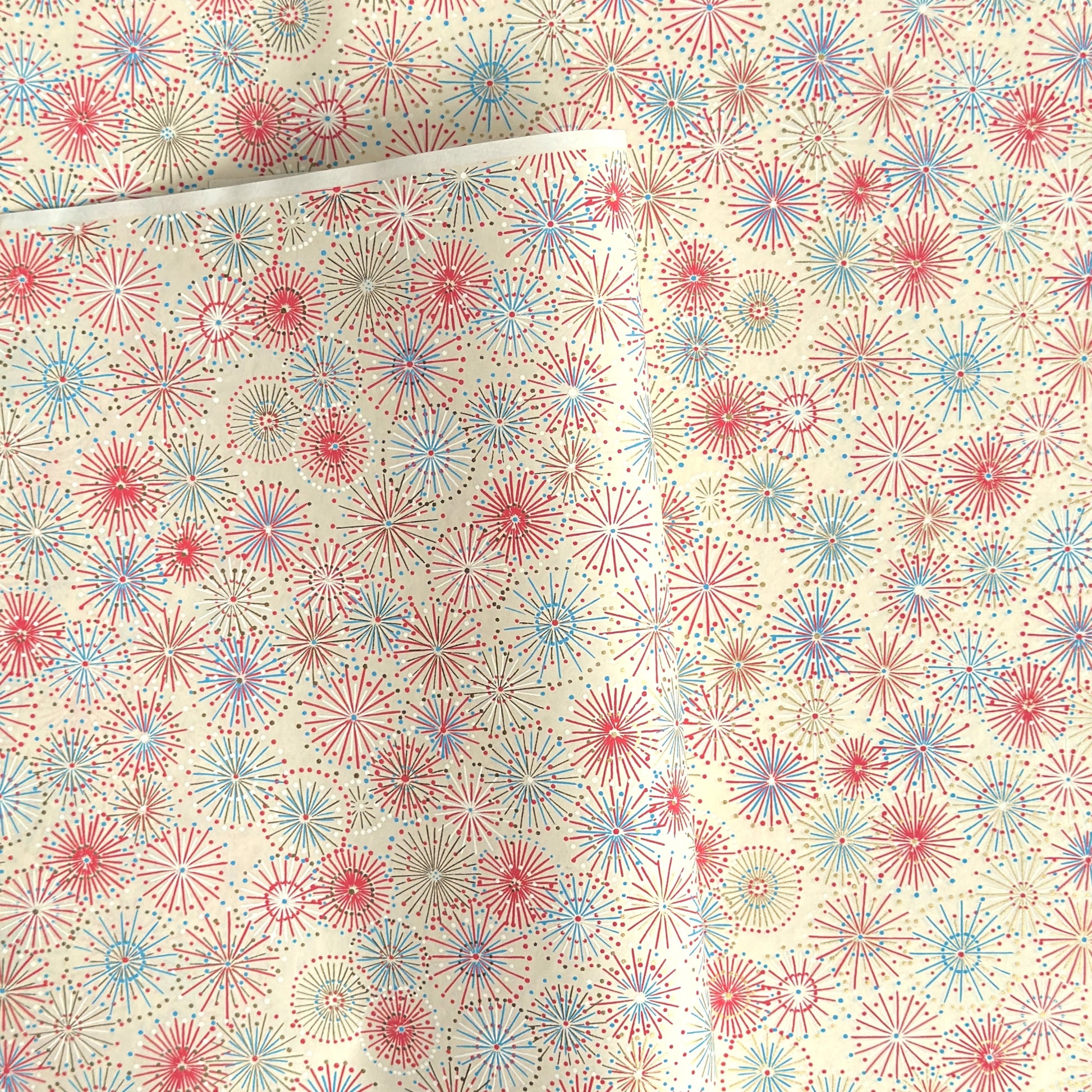 japanese chiyogami silkscreen printed paper with a pattern of fireworks in reds, pinks and lilacs on an ivory background.