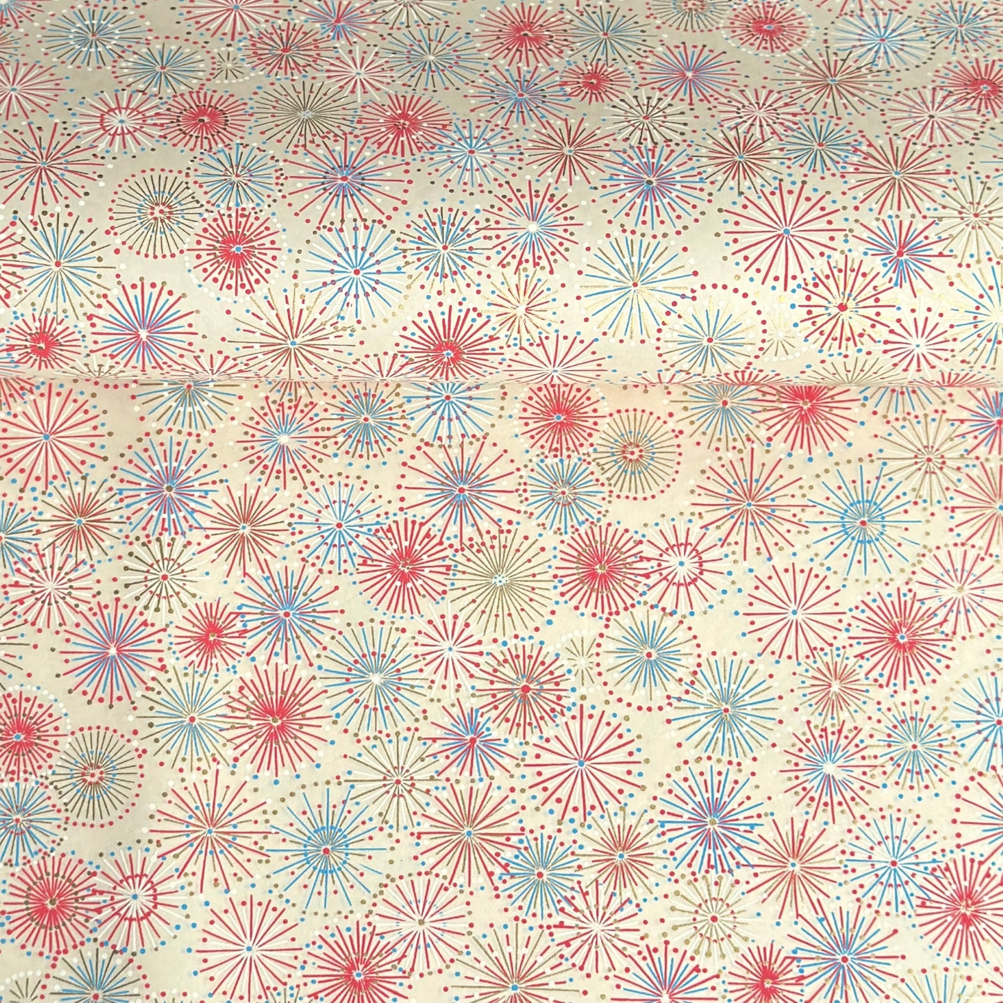 japanese chiyogami silkscreen printed paper with a pattern of fireworks in reds, pinks and lilacs on an ivory background.