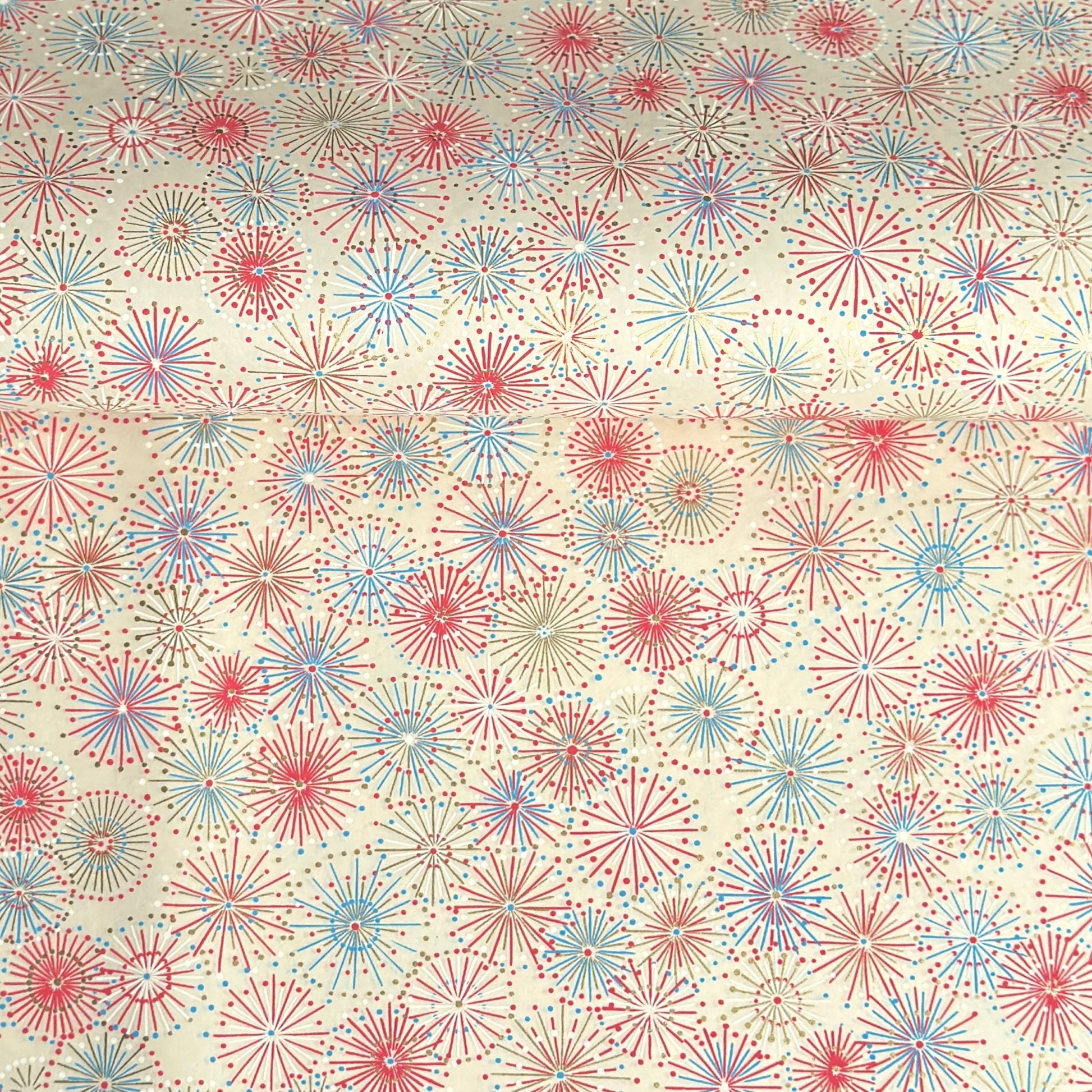 japanese chiyogami silkscreen printed paper with a pattern of fireworks in reds, pinks and lilacs on an ivory background.