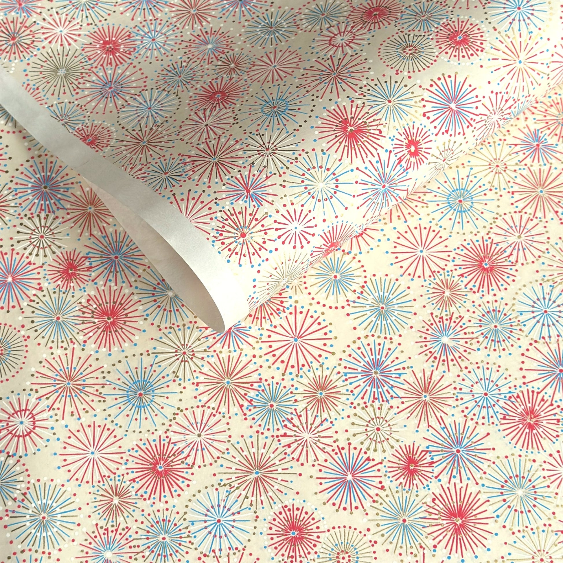 japanese chiyogami silkscreen printed paper with a pattern of fireworks in reds, pinks and lilacs on an ivory background.