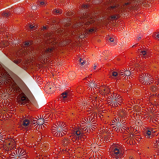 japanese chiyogami silkscreen printed paper with a pattern of fireworks in golds and purples on a red background.