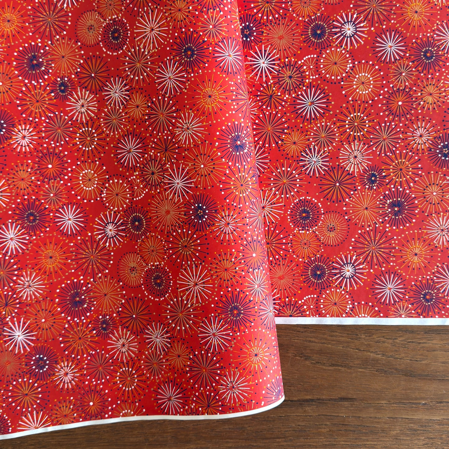 japanese chiyogami silkscreen printed paper with a pattern of fireworks in golds and purples on a red background.