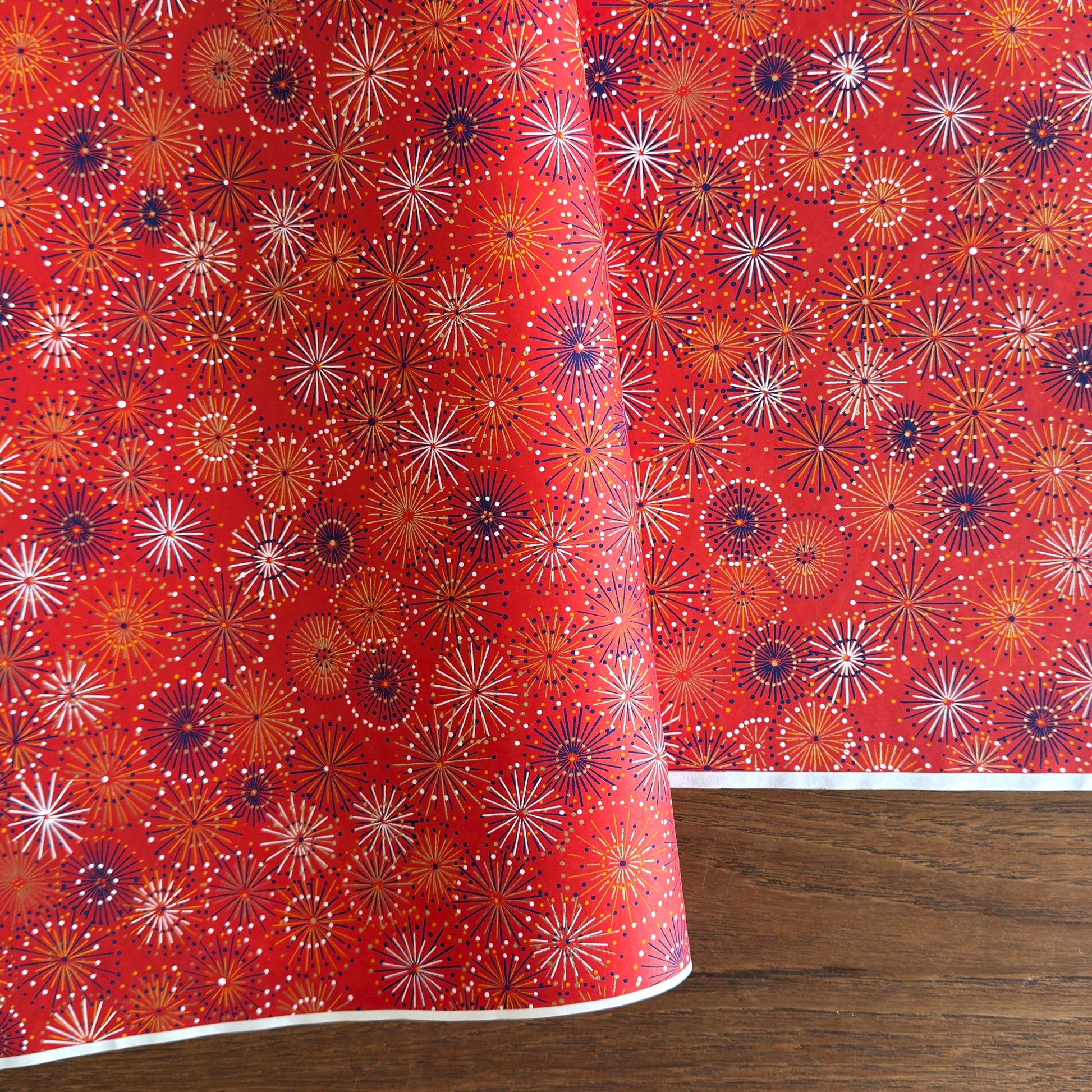 japanese chiyogami silkscreen printed paper with a pattern of fireworks in golds and purples on a red background.