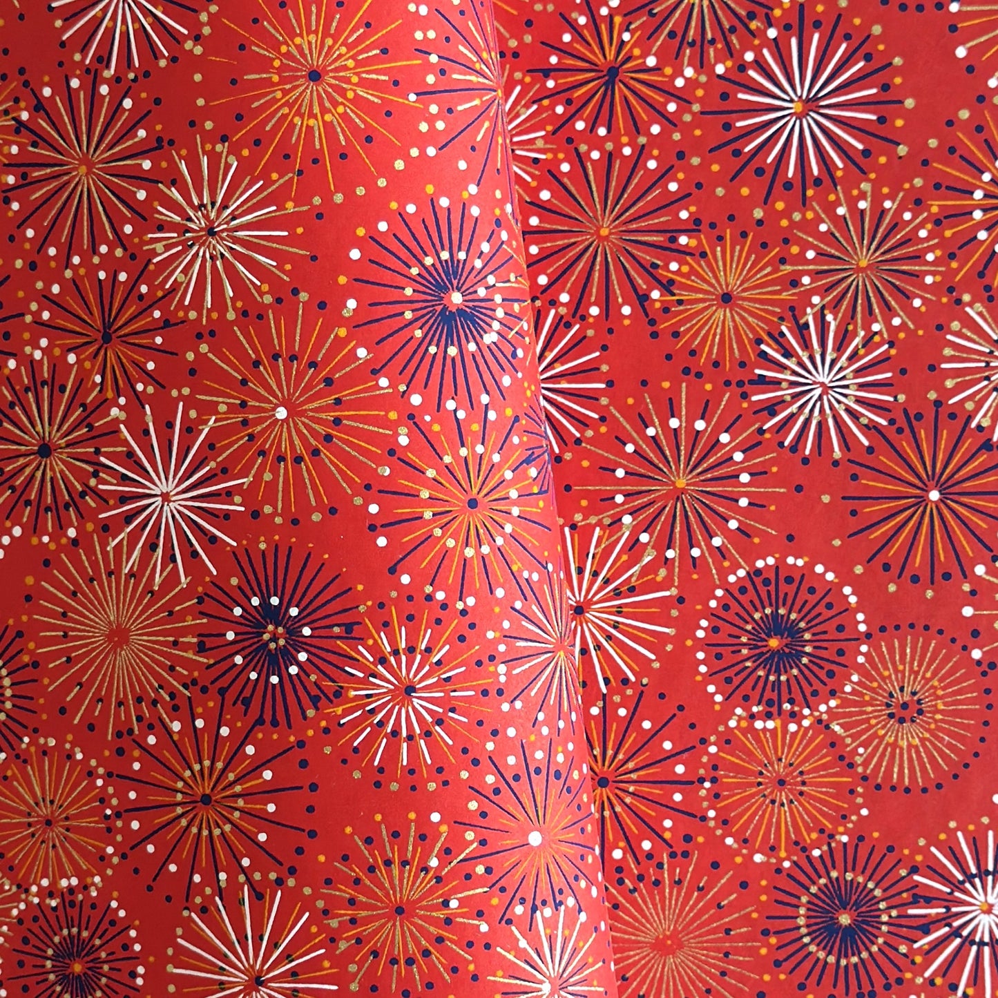 japanese chiyogami silkscreen printed paper with a pattern of fireworks in golds and purples on a red background.