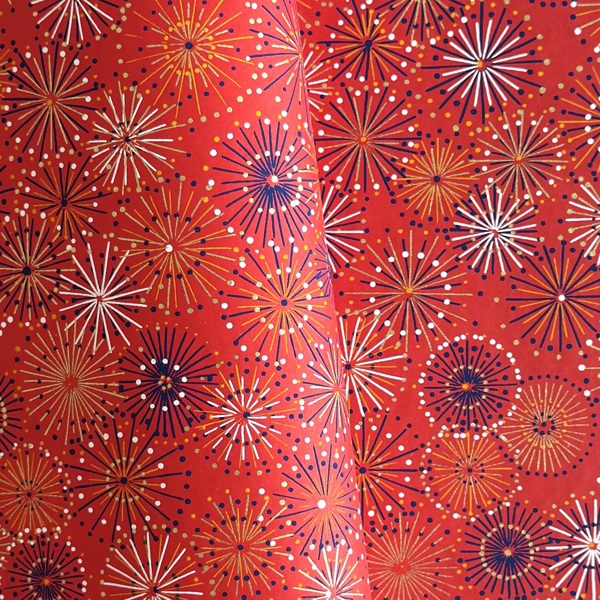 japanese chiyogami silkscreen printed paper with a pattern of fireworks in golds and purples on a red background.