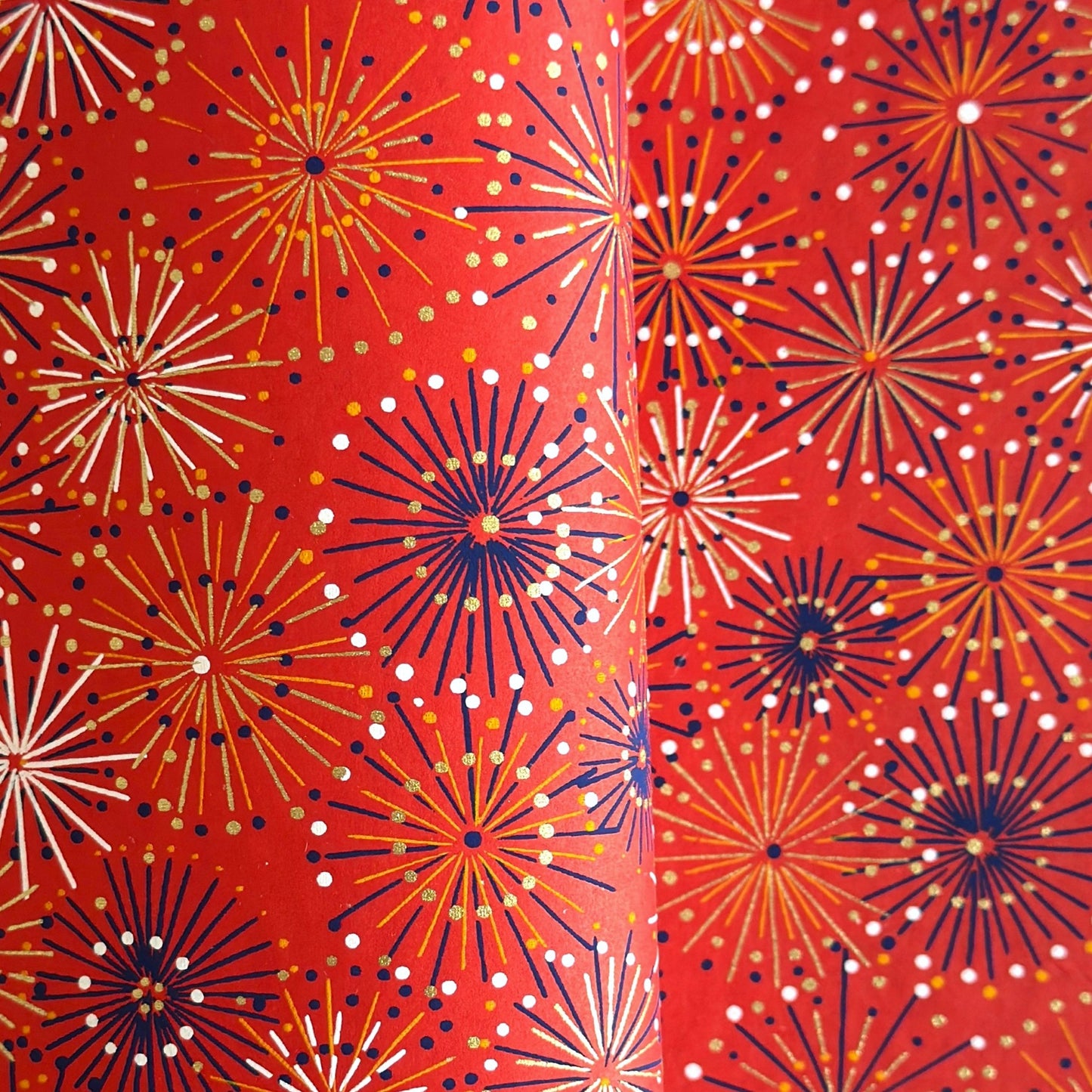 japanese chiyogami silkscreen printed paper with a pattern of fireworks in golds and purples on a red background.