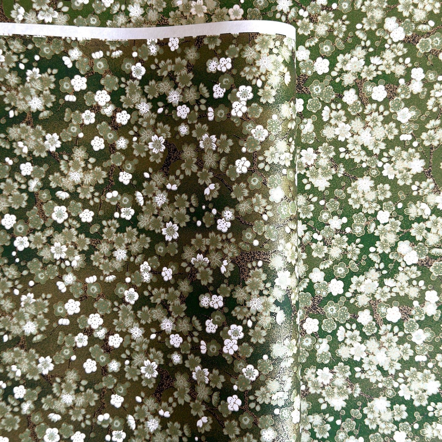 Japanese chiyogami paper with white and pale green blossom flowers on dark green backdrop.