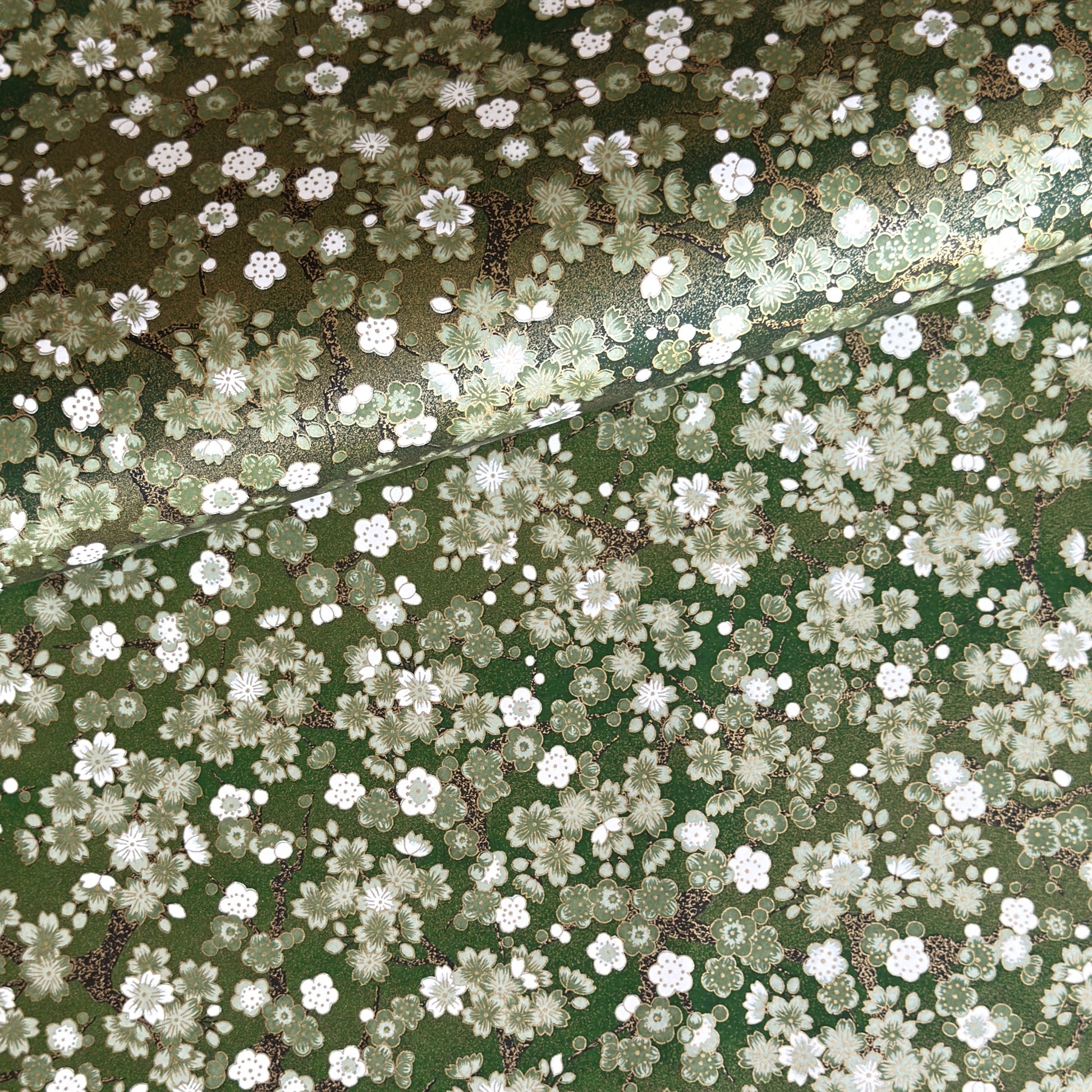Japanese chiyogami paper with white and pale green blossom flowers on dark green backdrop.