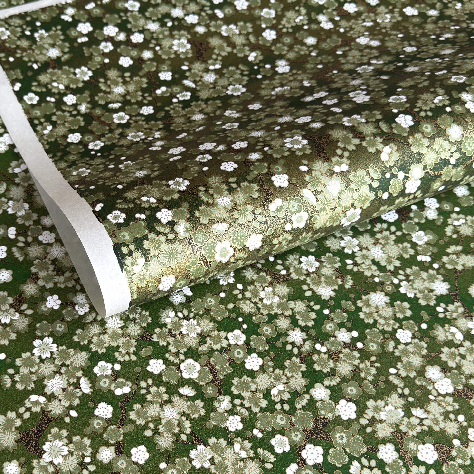 Japanese chiyogami paper with white and pale green blossom flowers on dark green backdrop.