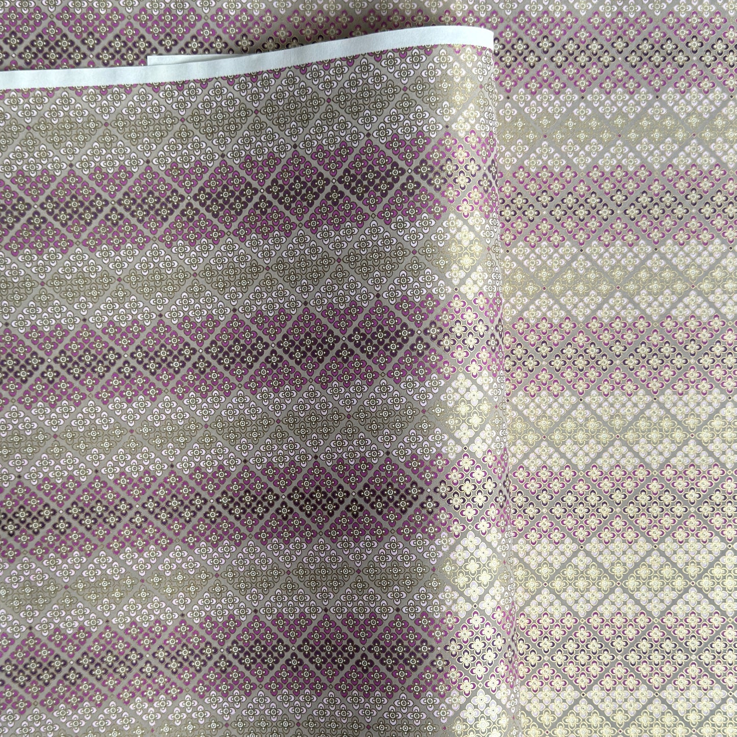 Japanese chiyogami silkscreen printed paper with rows of small flower motifs in purple, lilac and white on a taupe background with gold accents.