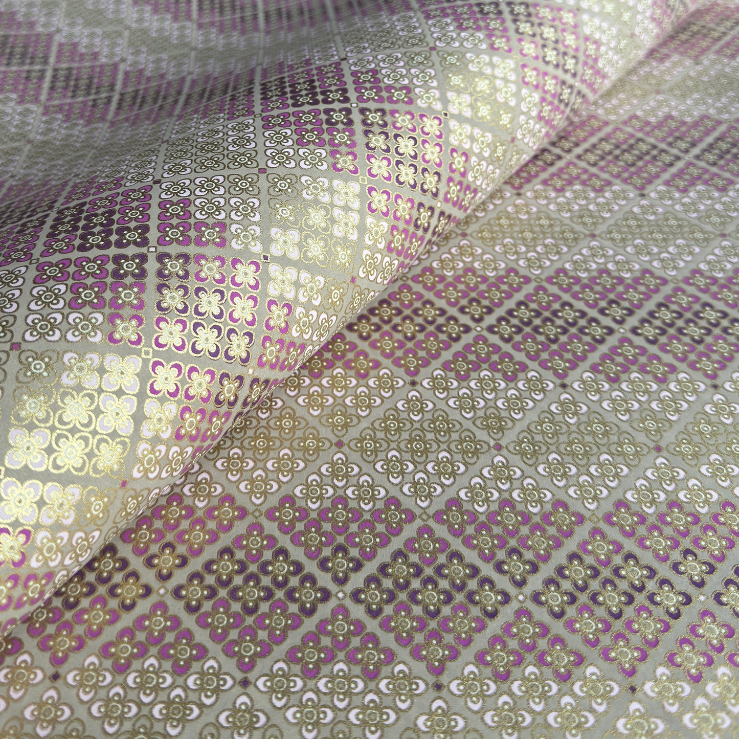 Japanese chiyogami silkscreen printed paper with rows of small flower motifs in purple, lilac and white on a taupe background with gold accents.