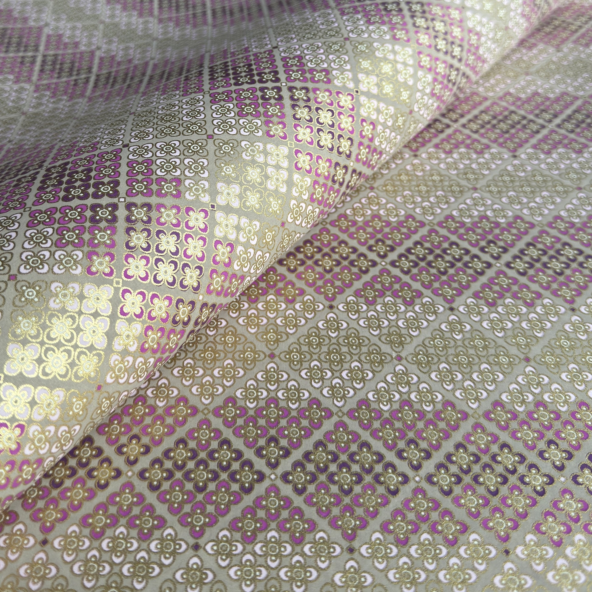Japanese chiyogami silkscreen printed paper with rows of small flower motifs in purple, lilac and white on a taupe background with gold accents.