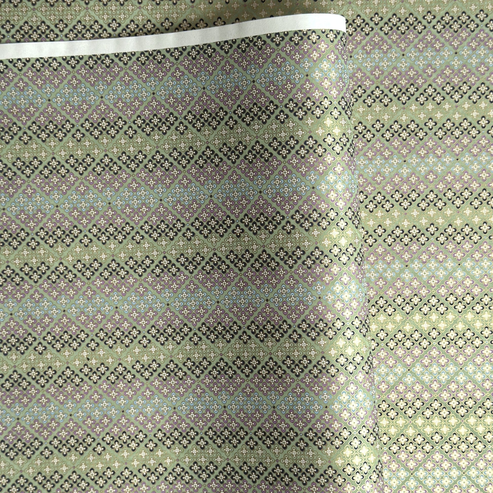 Japanese silkscreen chiyogami paper with a repeat pattern of stripes of a small floral motif in black, lilac and blue on a moss green backdrop