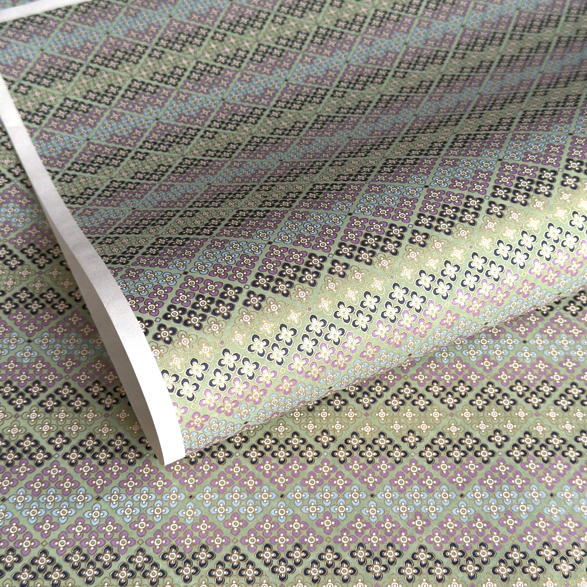 Japanese silkscreen chiyogami paper with a repeat pattern of stripes of a small floral motif in black, lilac and blue on a moss green backdrop