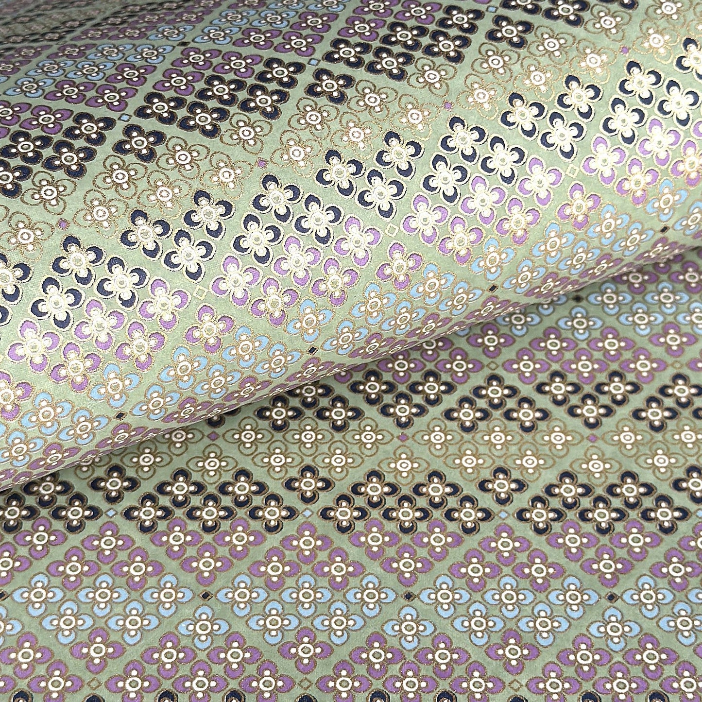 Japanese silkscreen chiyogami paper with a repeat pattern of stripes of a small floral motif in black, lilac and blue on a moss green backdrop