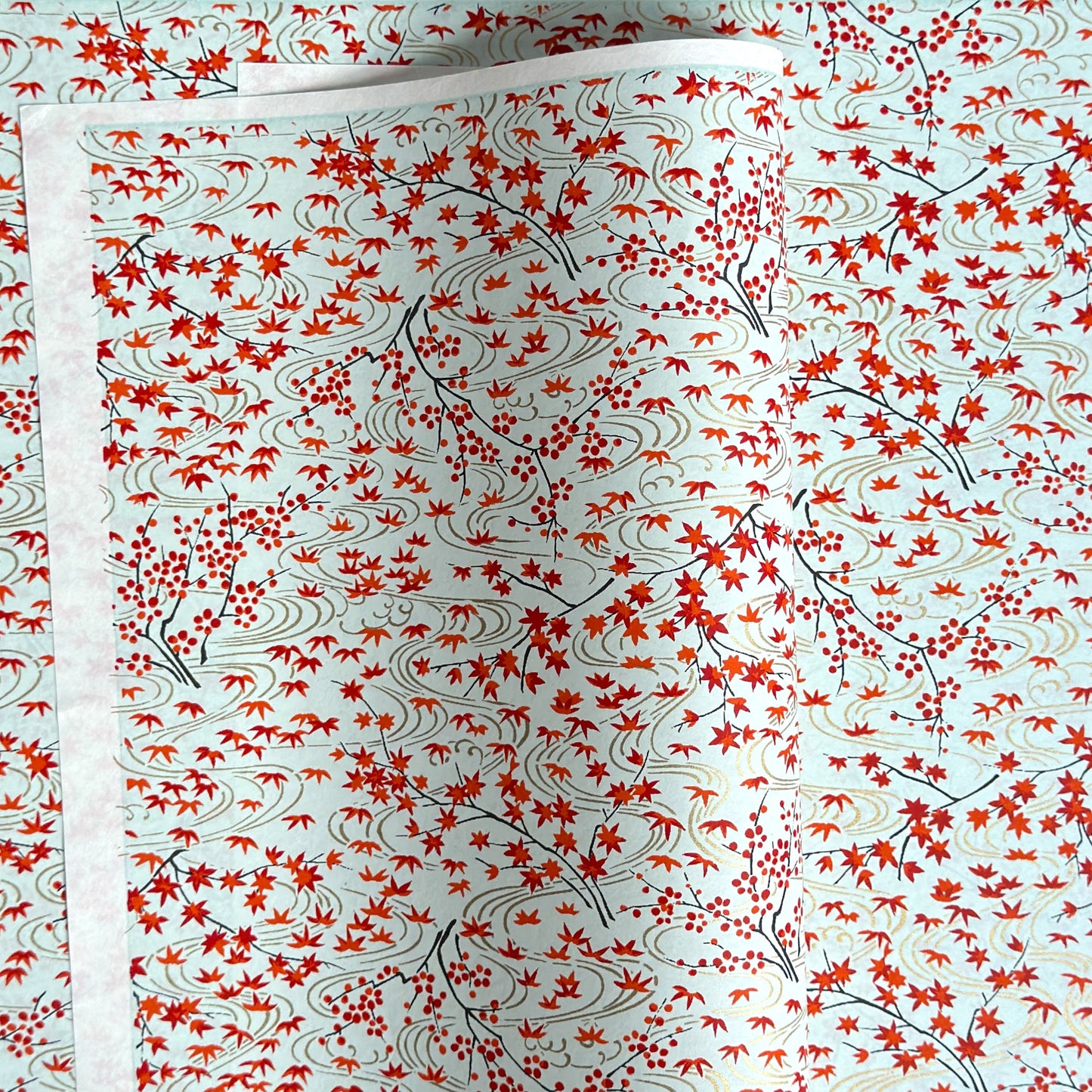 a sheet of japanese silkscreen printed chiyogami paper with a pattern of gold rivers, red falling leaves on a soft aqua background