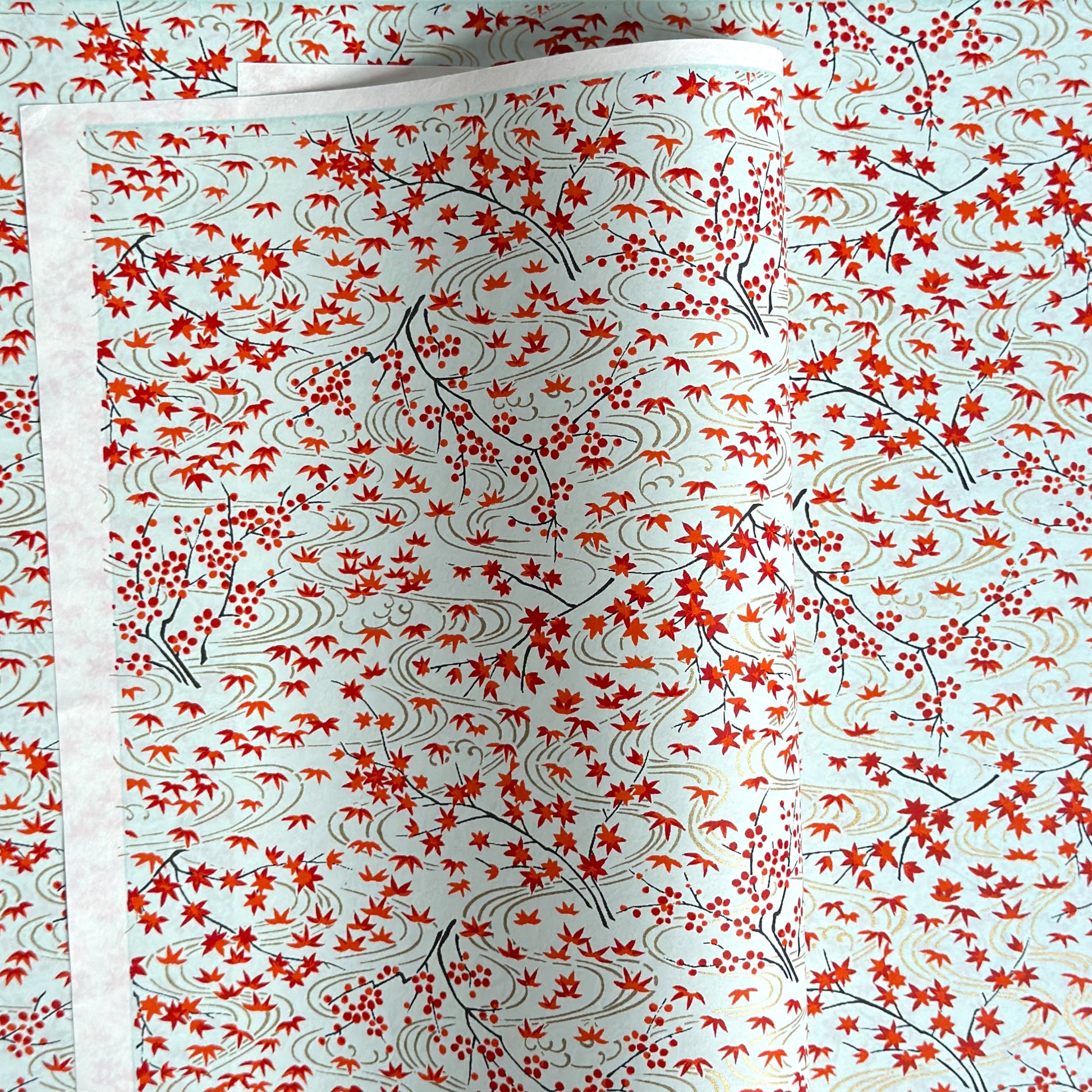 a sheet of japanese silkscreen printed chiyogami paper with a pattern of gold rivers, red falling leaves on a soft aqua background