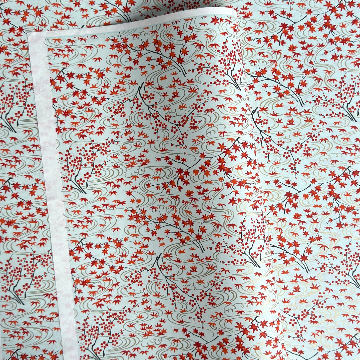 a sheet of japanese silkscreen printed chiyogami paper with a pattern of gold rivers, red falling leaves on a soft aqua background