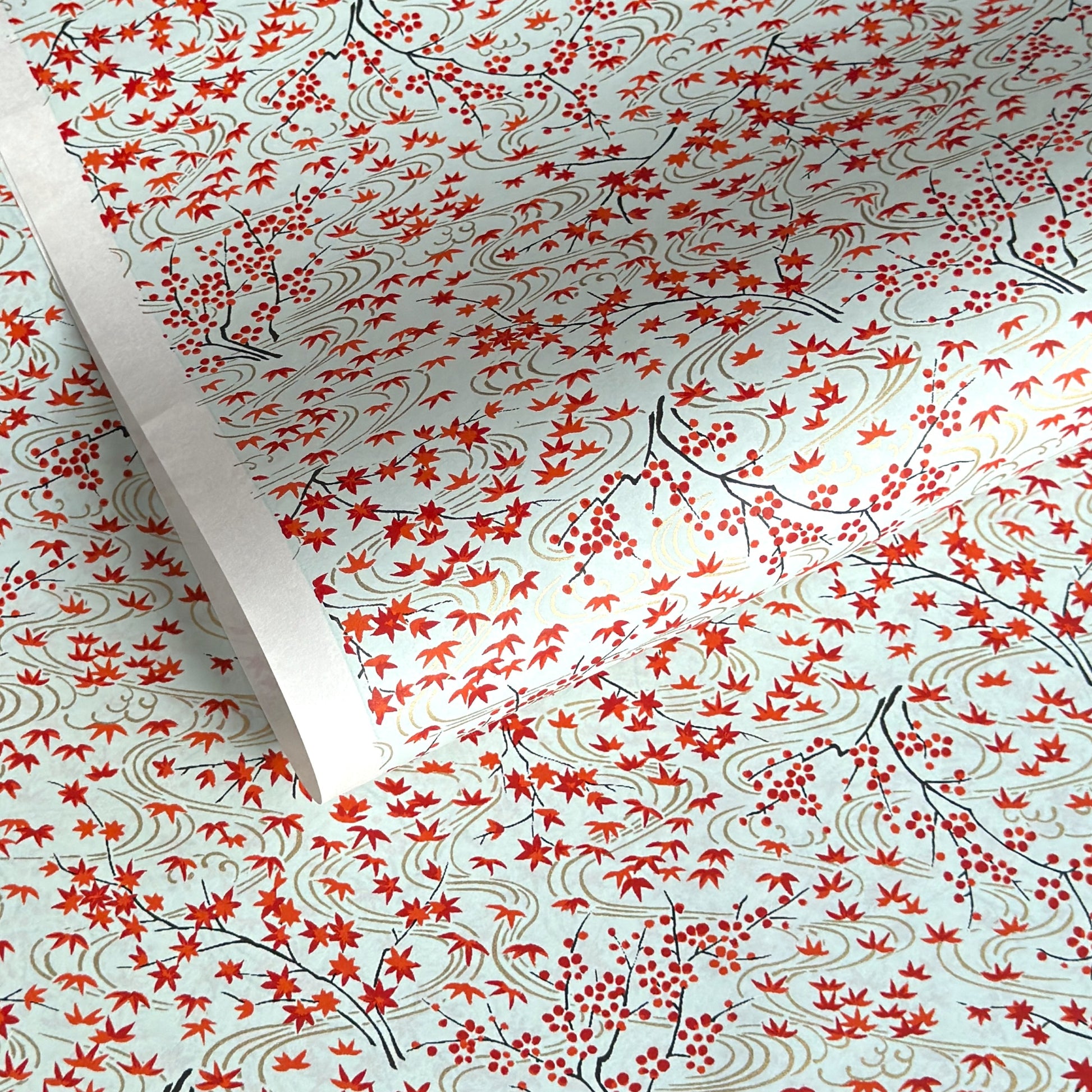 a sheet of japanese silkscreen printed chiyogami paper with a pattern of gold rivers, red falling leaves on a soft aqua background