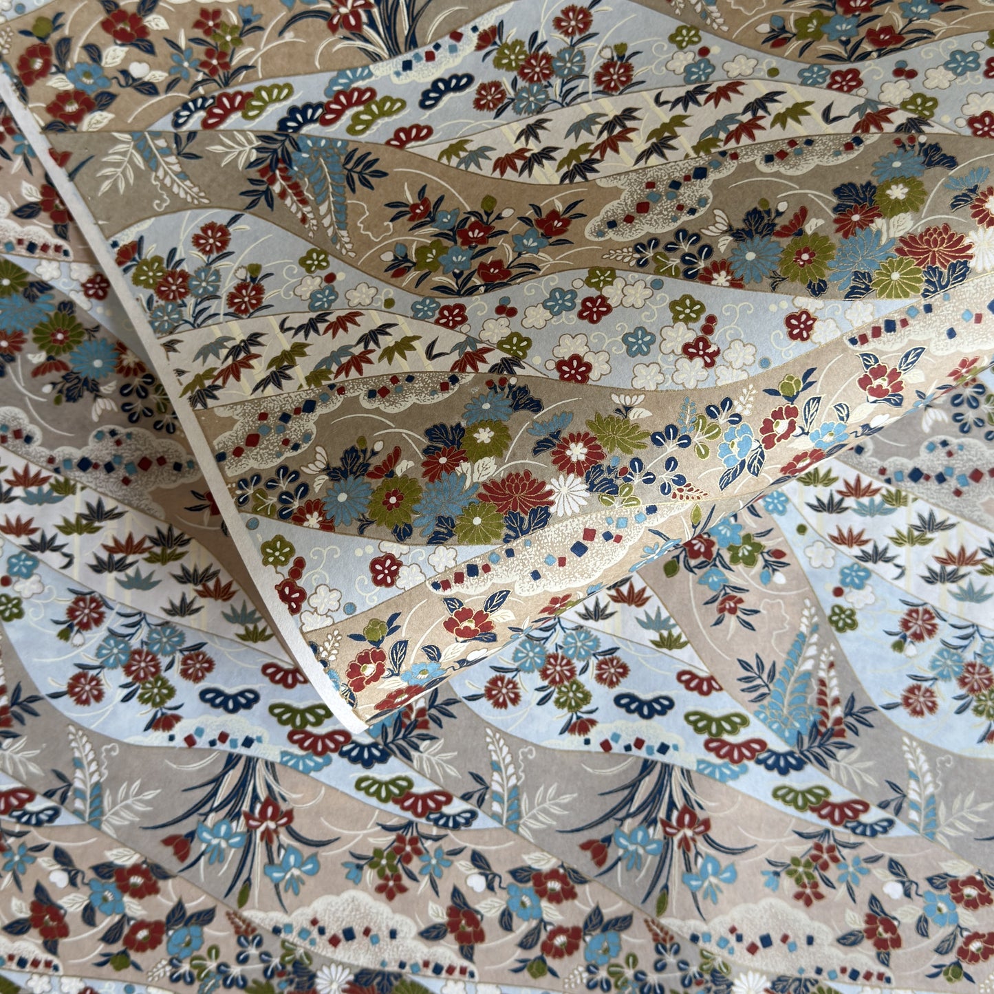 japanese silk-screen handmade paper showing taupe and pale blue waves pattern with multicolour flowers and foliage, with gold accents