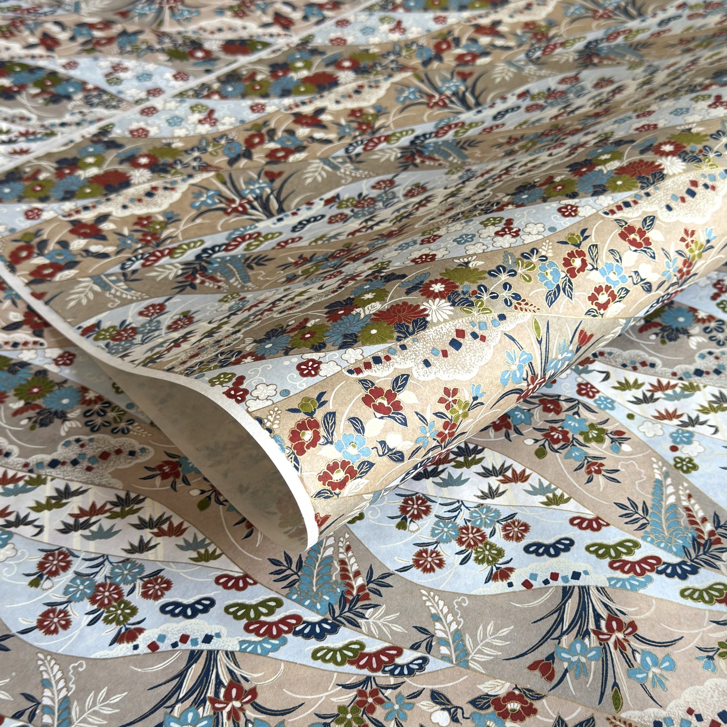 japanese silk-screen handmade paper showing taupe and pale blue waves pattern with multicolour flowers and foliage, with gold accents
