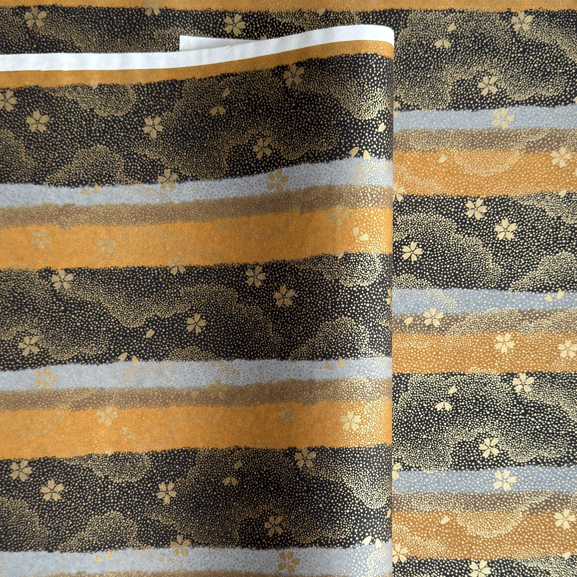 japanese chiyogami paper in stripes of black, brown, ochre and grey with gold clouds and flowers